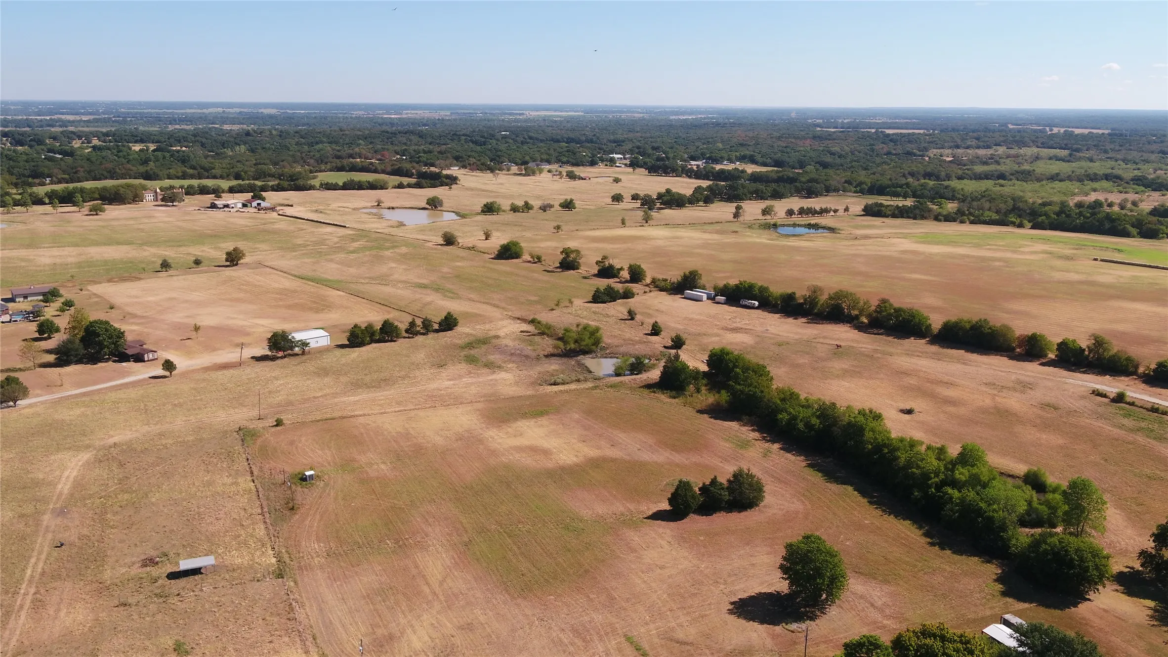 Expansive rural landscape featuring scattered structures, mature trees, and multiple ponds