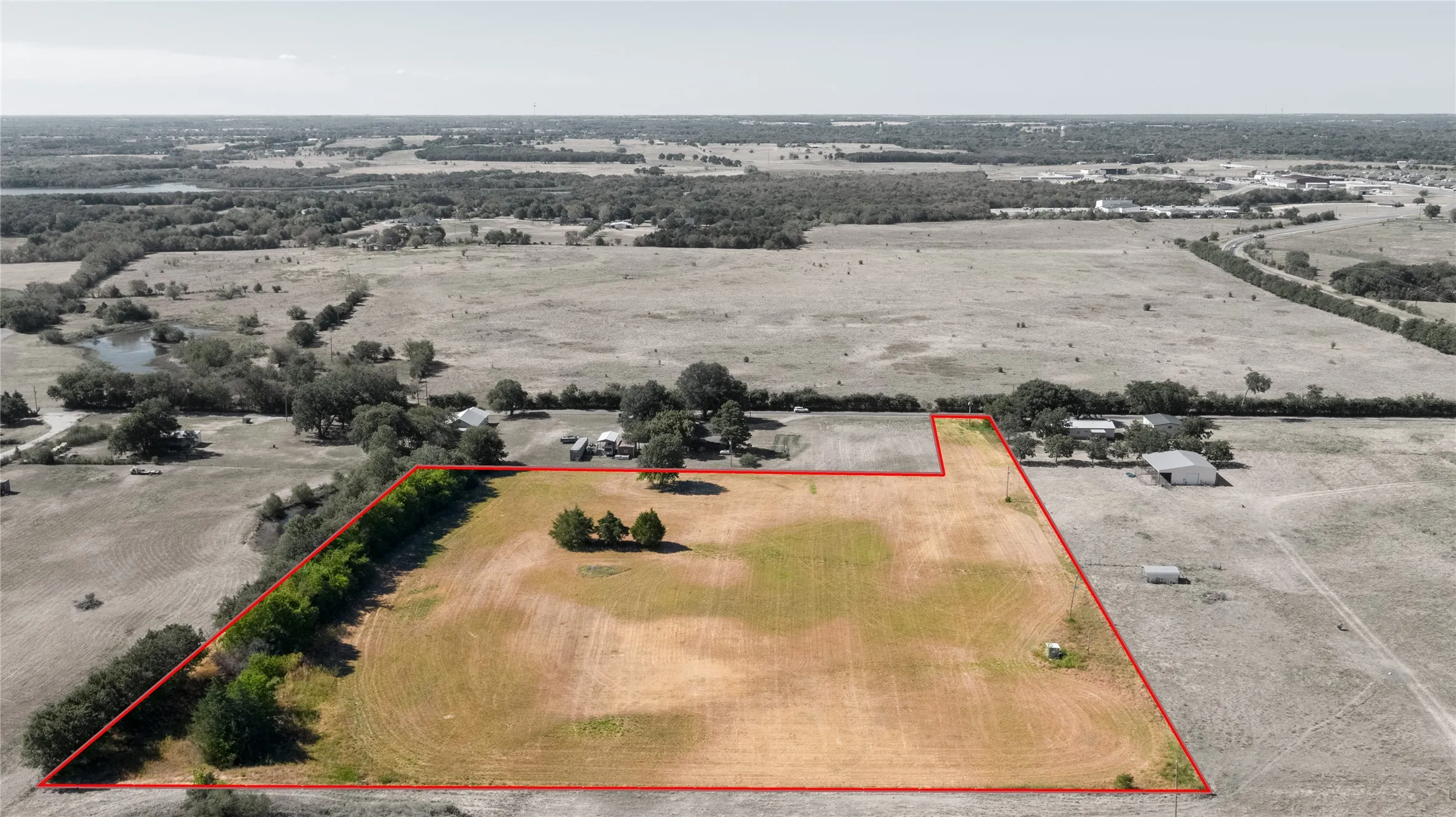 Expansive open land area with defined property lines, featuring scattered trees and natural vegetation