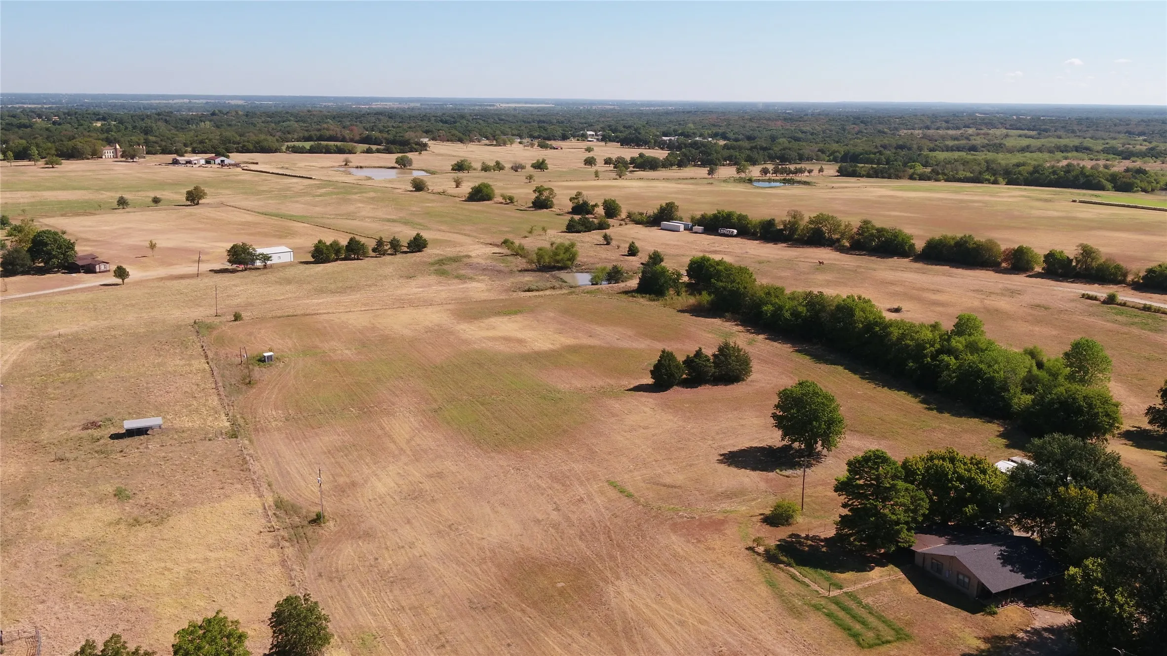 Expansive land parcel featuring open fields, scattered mature trees, and multiple outbuildings