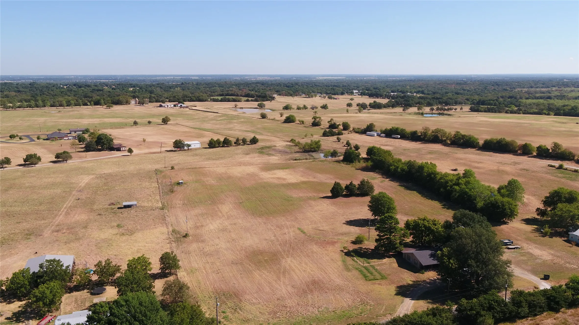 Expansive rural landscape featuring scattered trees, open fields, and distant structures