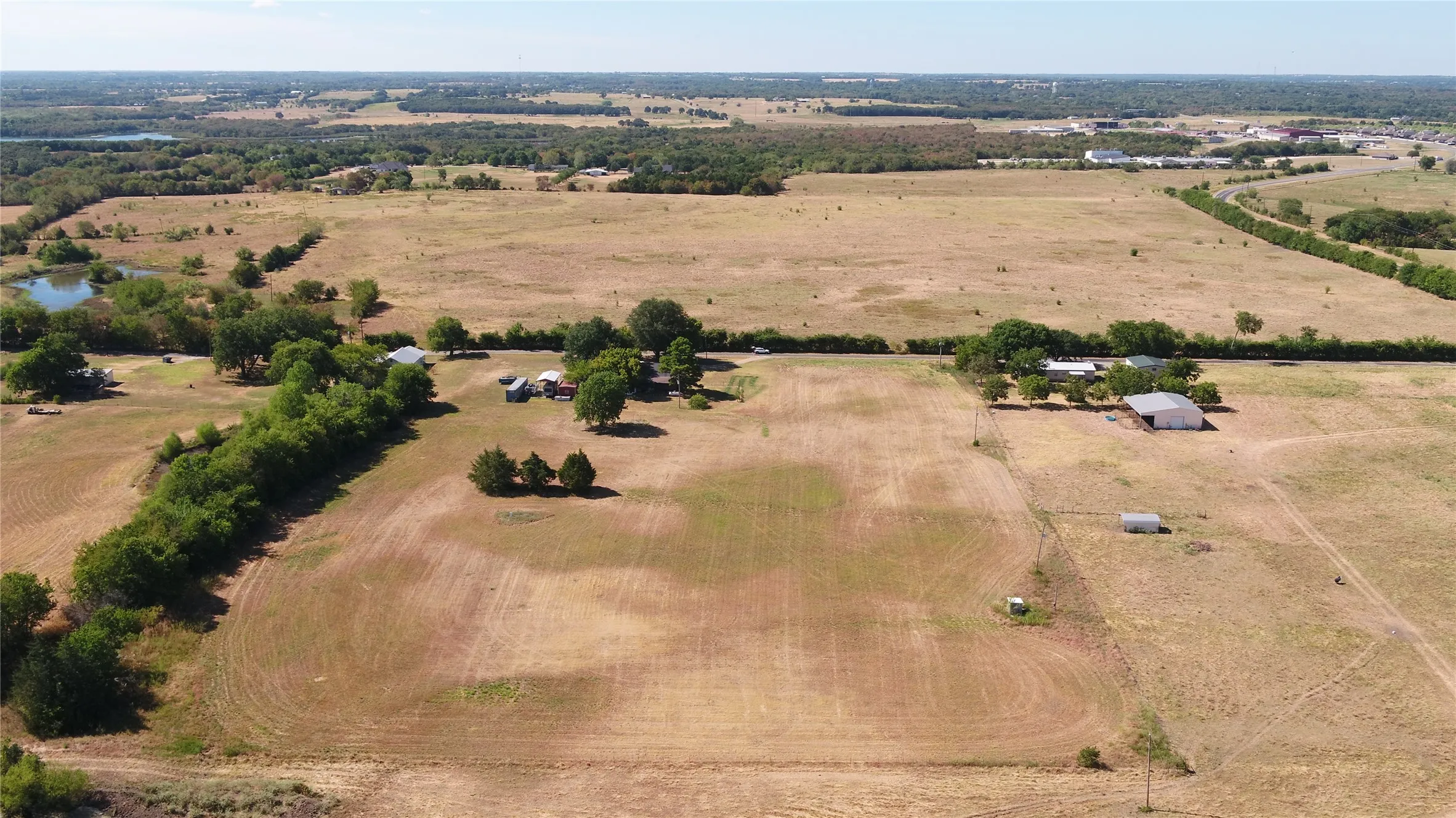 Expansive land parcel with multiple structures, including a primary residence and outbuildings, surrounded by open fields and mature trees
