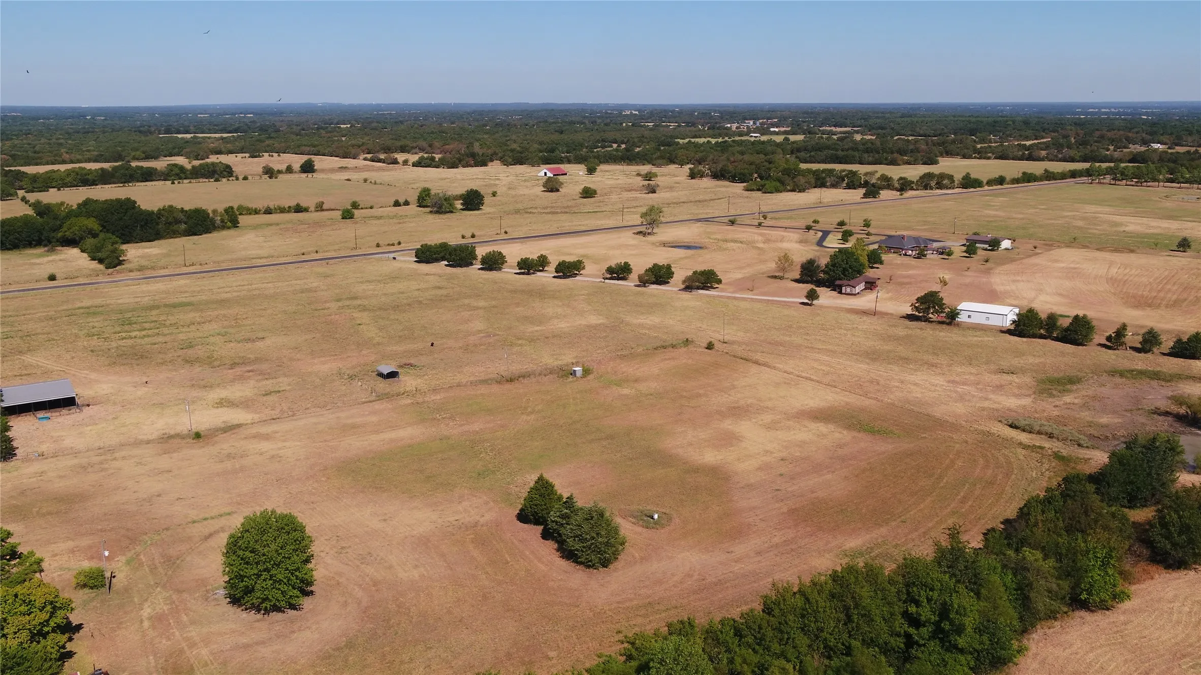 Expansive acreage featuring multiple structures, a paved road, and scattered trees