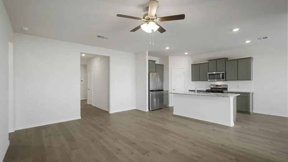Open-concept living area featuring wood-finish flooring, a ceiling fan, a kitchen island with a stone countertop, grey cabinetry, and stainless steel appliances