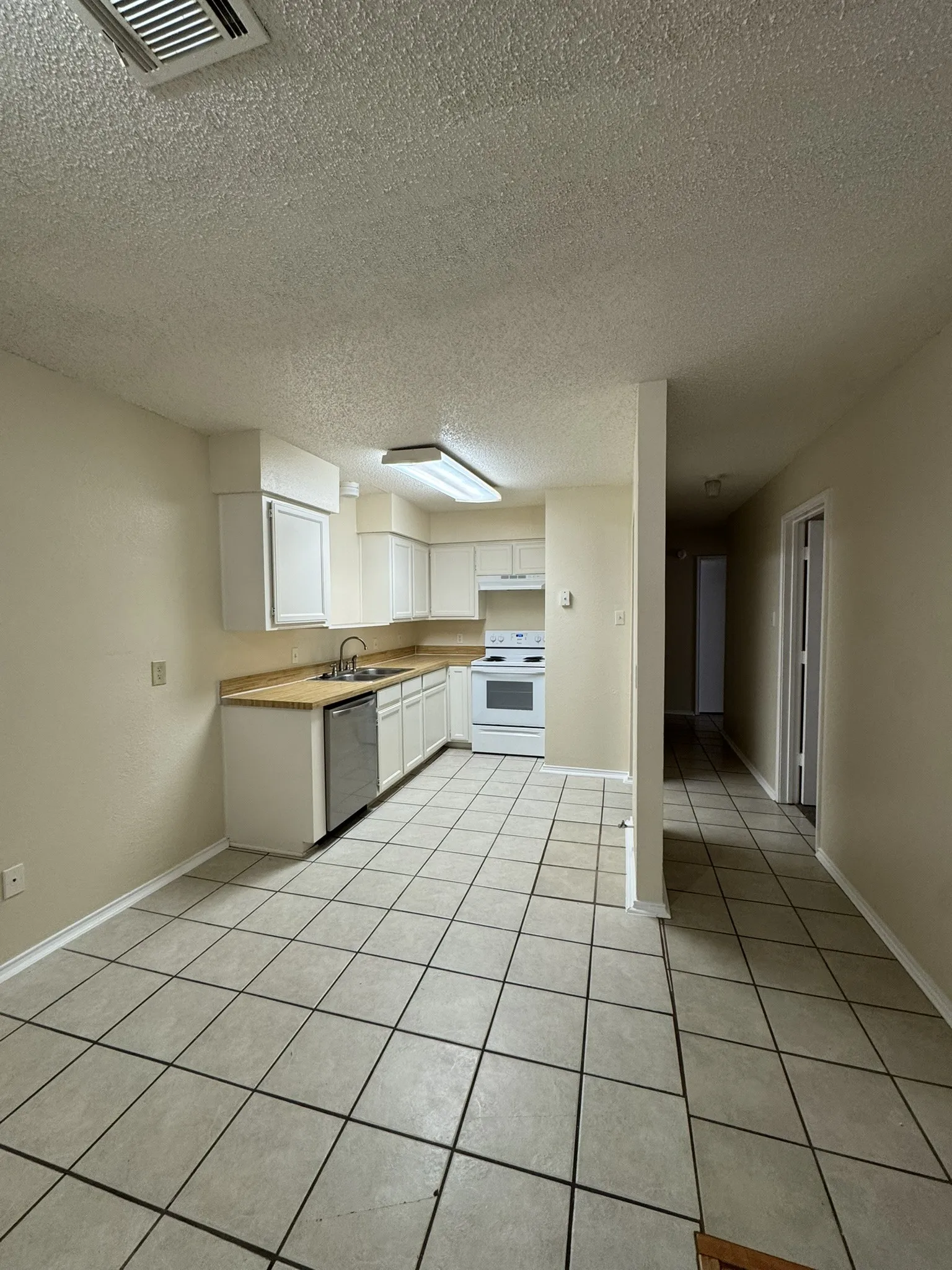 Kitchen with electric range, stainless steel dishwasher, a textured ceiling, white cabinets, and light countertops