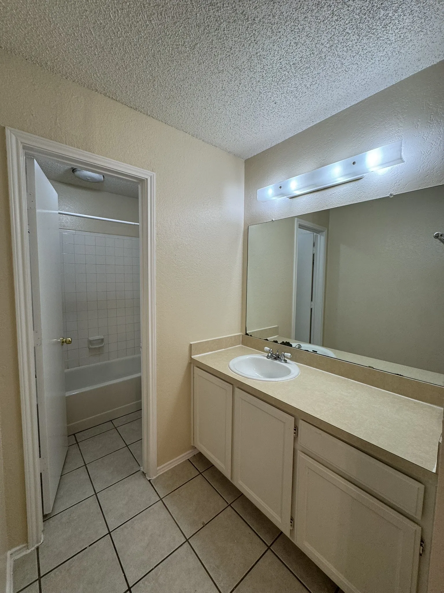 Full bath with tile patterned flooring, vanity, a textured ceiling, and tub / shower combination
