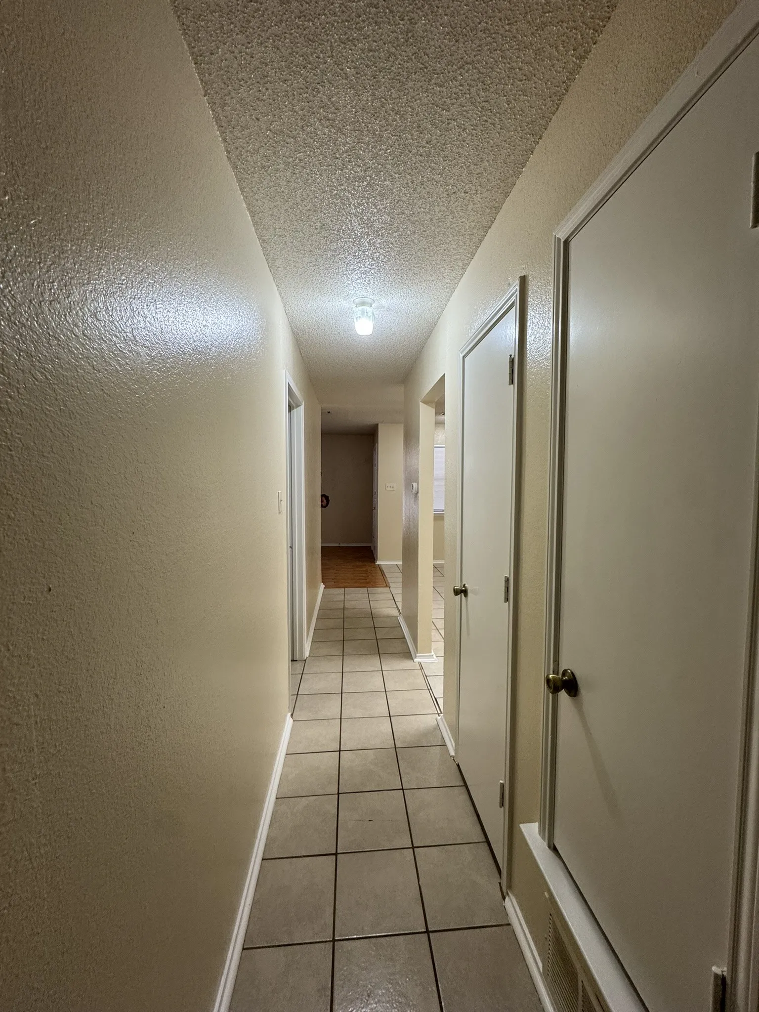 Hallway with light tile patterned floors, a textured ceiling, and a textured wall