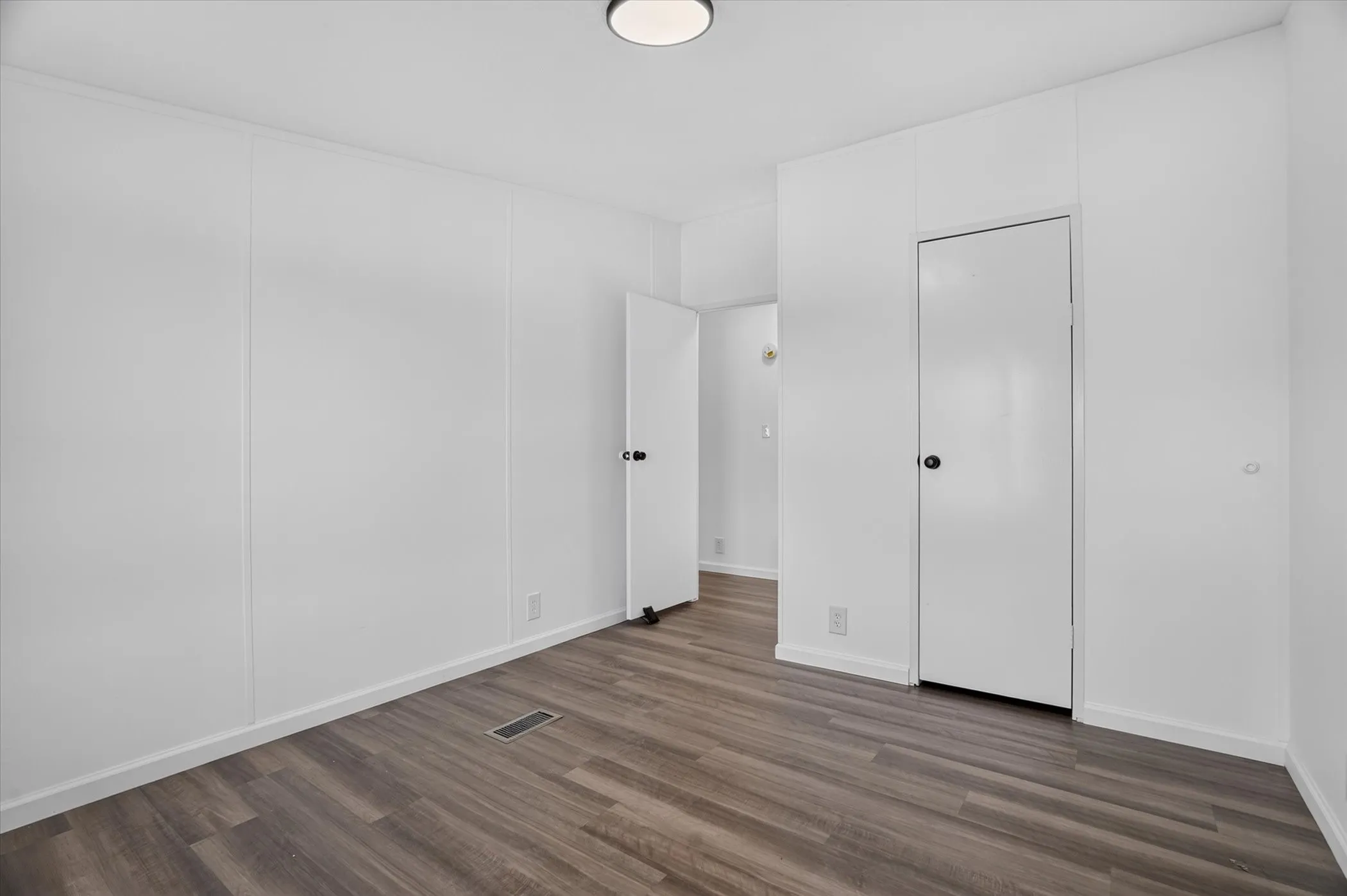 White walls with vertical paneling, wood-finish flooring, white trim, and a flush mount ceiling light
