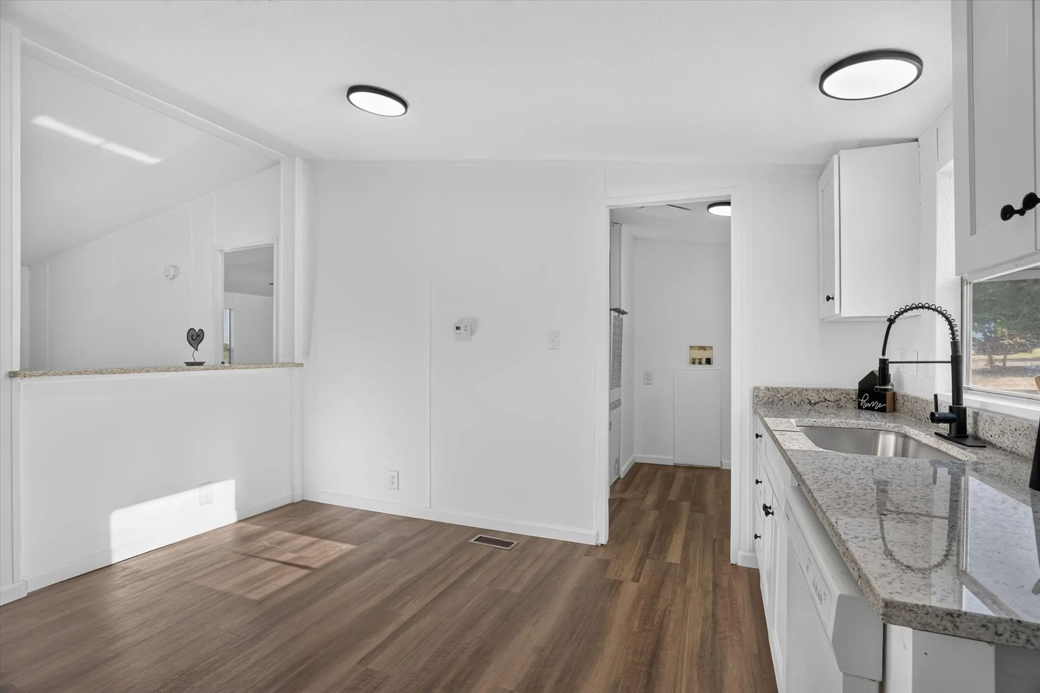 Kitchen featuring a stainless steel sink, black gooseneck faucet, light granite-style countertops, white cabinetry, and wood-finish flooring