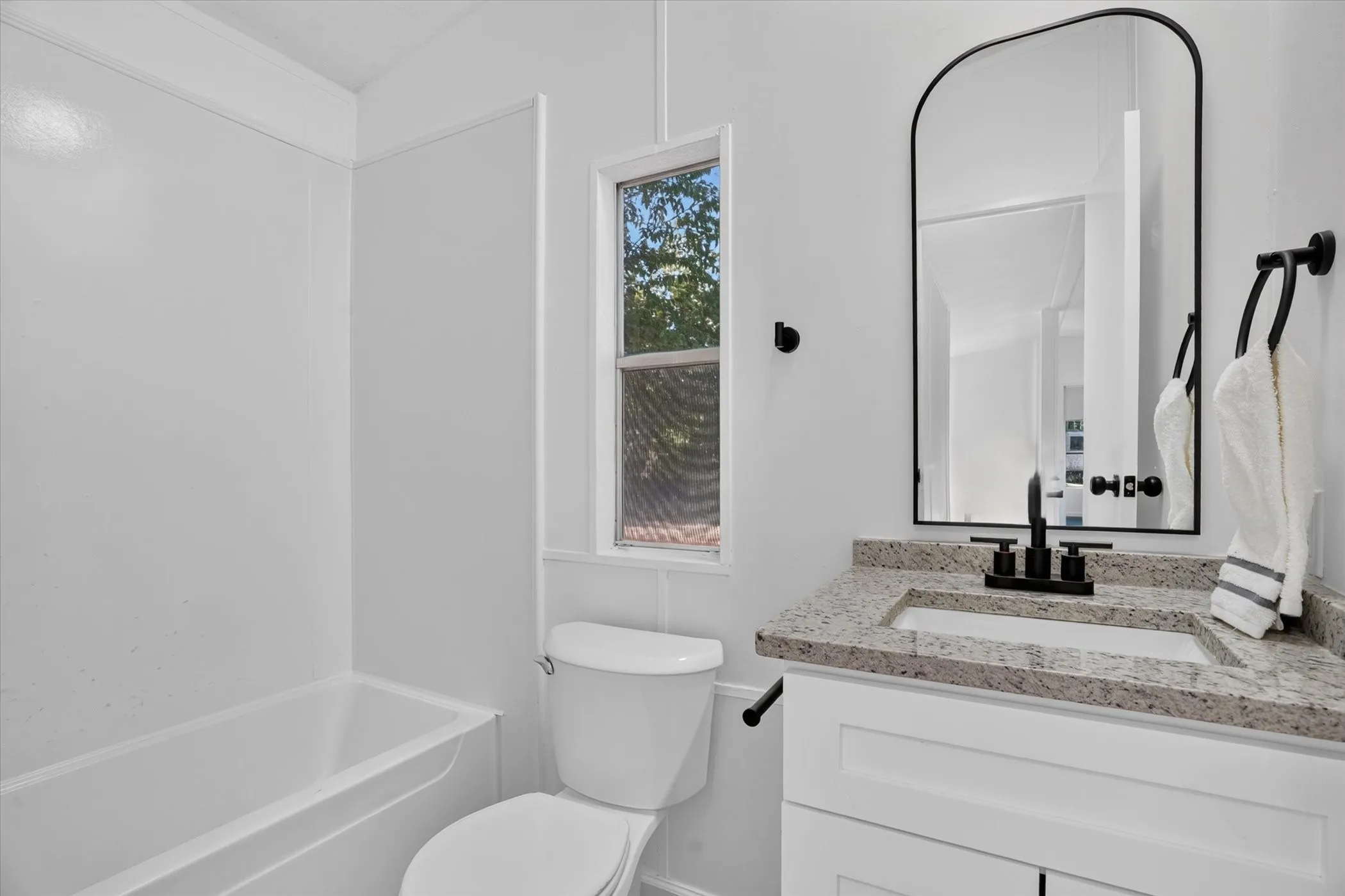 White vanity with a stone countertop, an undermount sink, and a black faucet