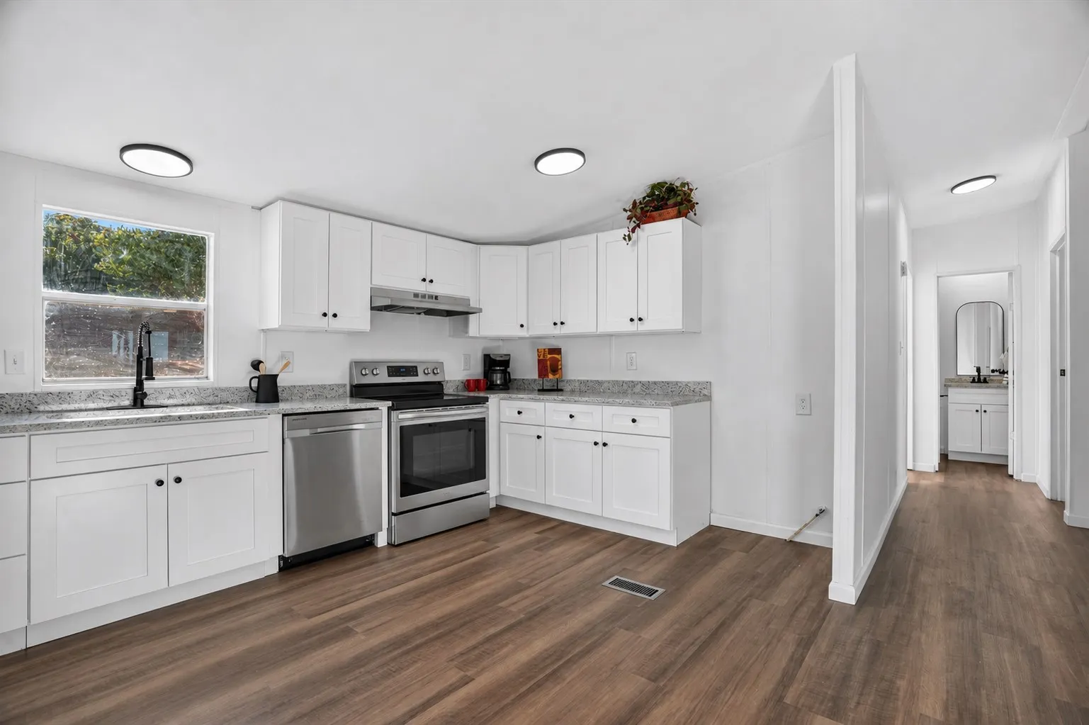 Kitchen featuring white cabinetry, light-toned countertops, stainless steel appliances, and wood-finish flooring