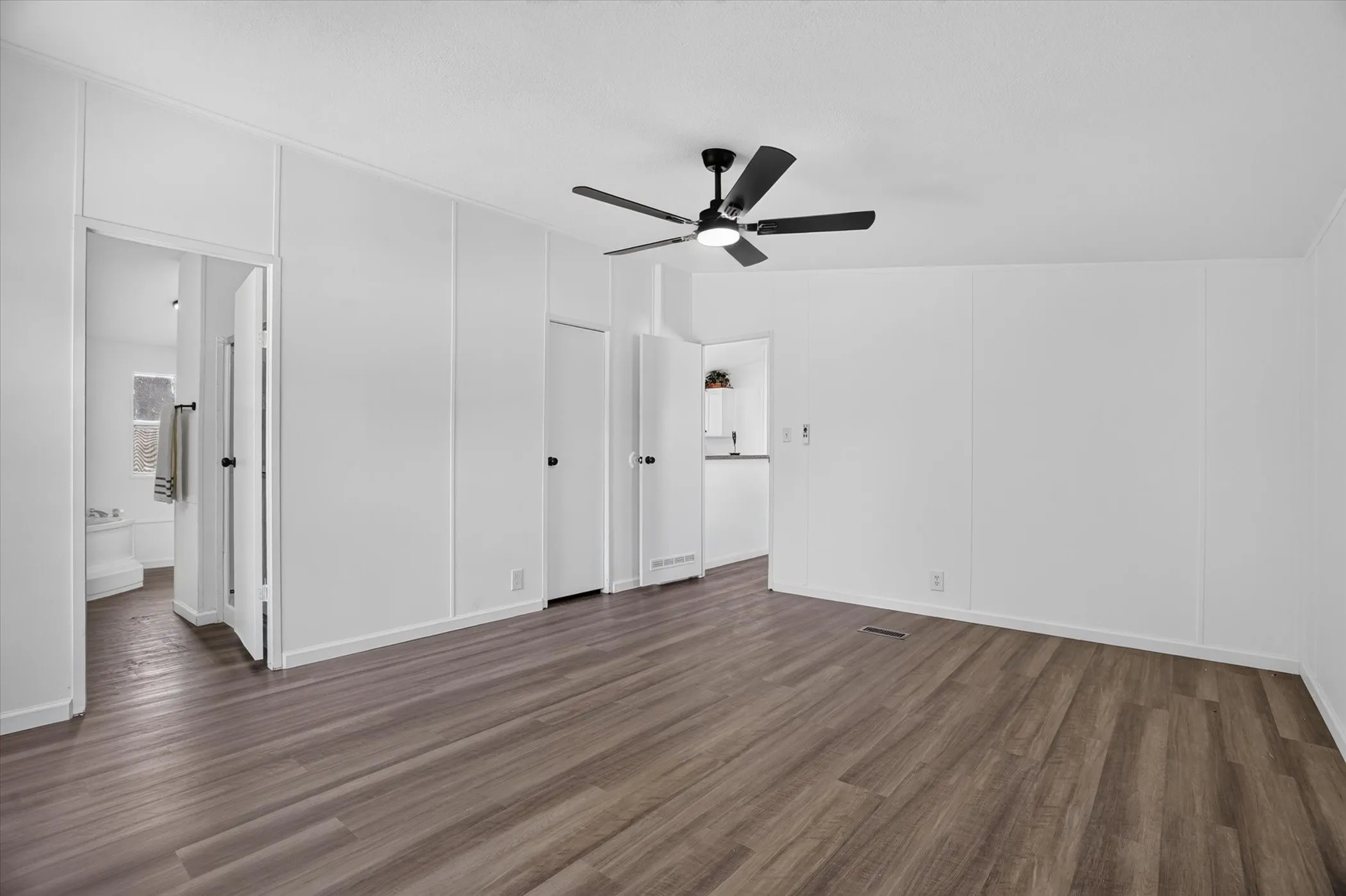 Spacious room featuring wood-finish flooring, a contemporary ceiling fan, and crisp white walls