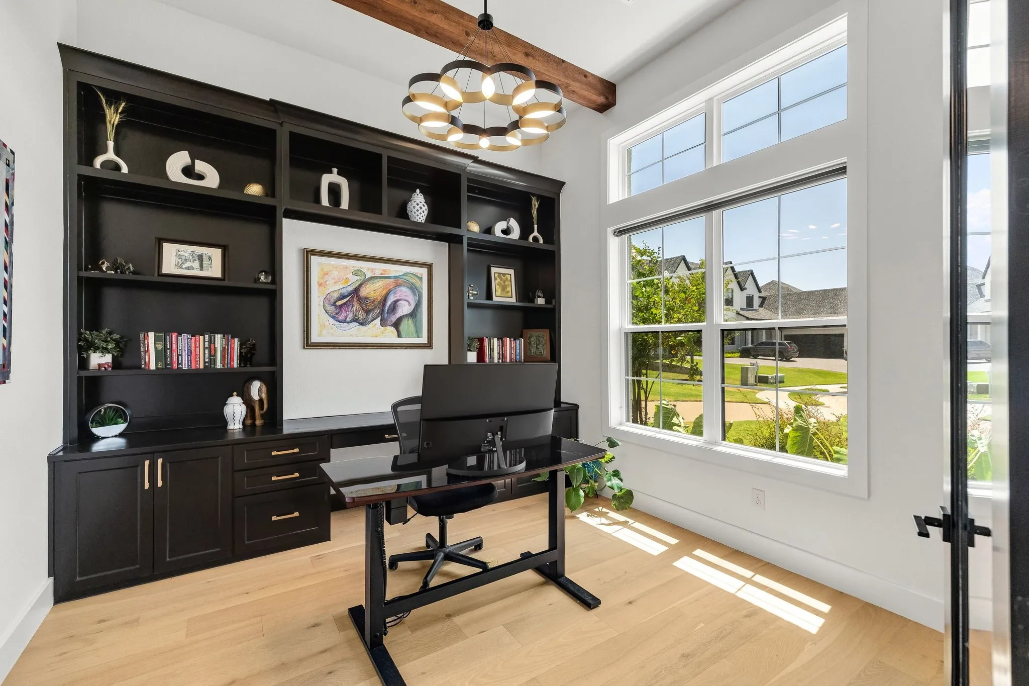 Custom built-in cabinetry with desk space, light wood-finish flooring, exposed wood beam, large windows, and a modern chandelier