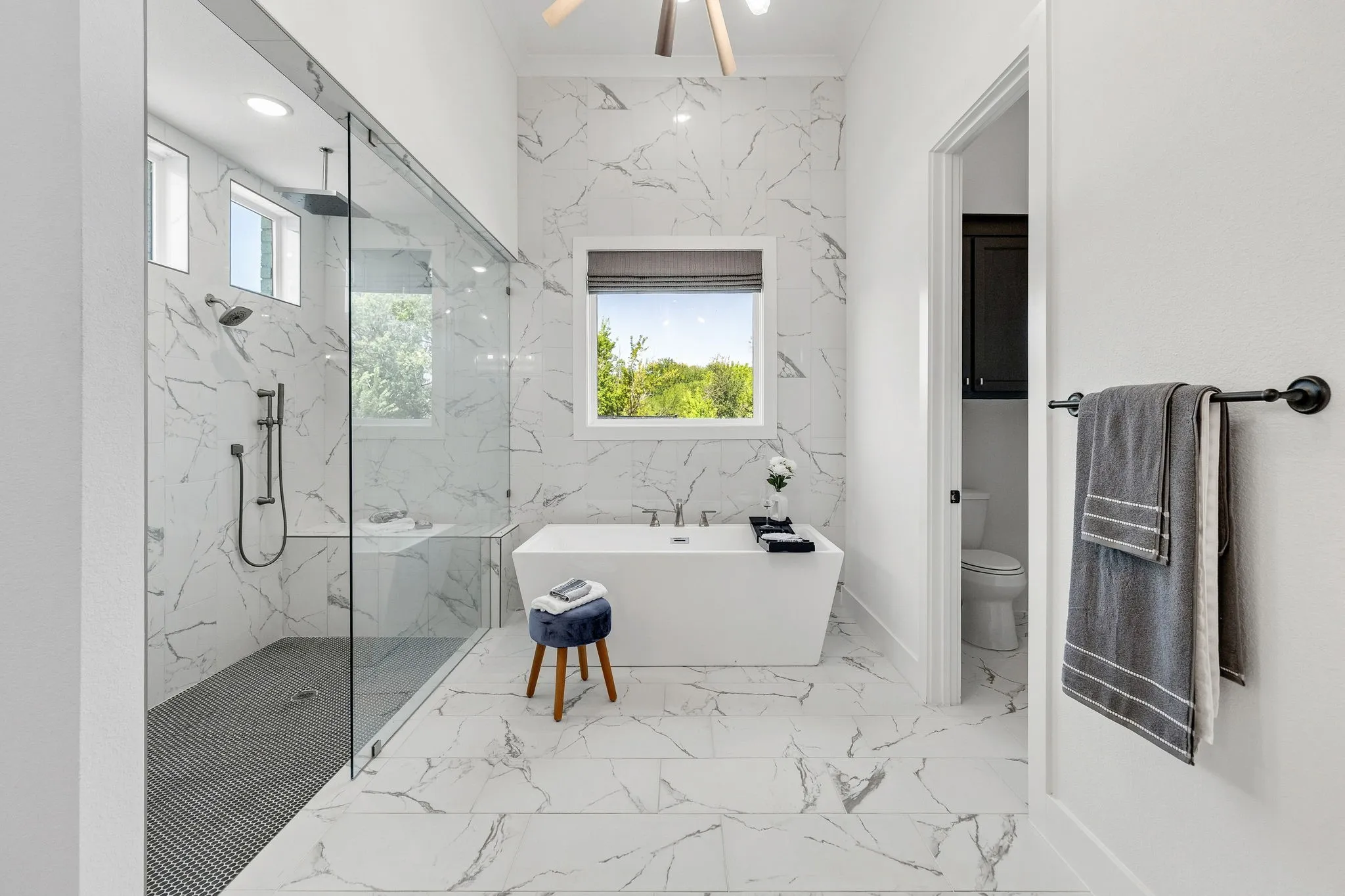 Spacious bathroom featuring a freestanding tub, large walk-in shower with glass enclosure, dual shower heads, and white marble-look tile flooring and walls