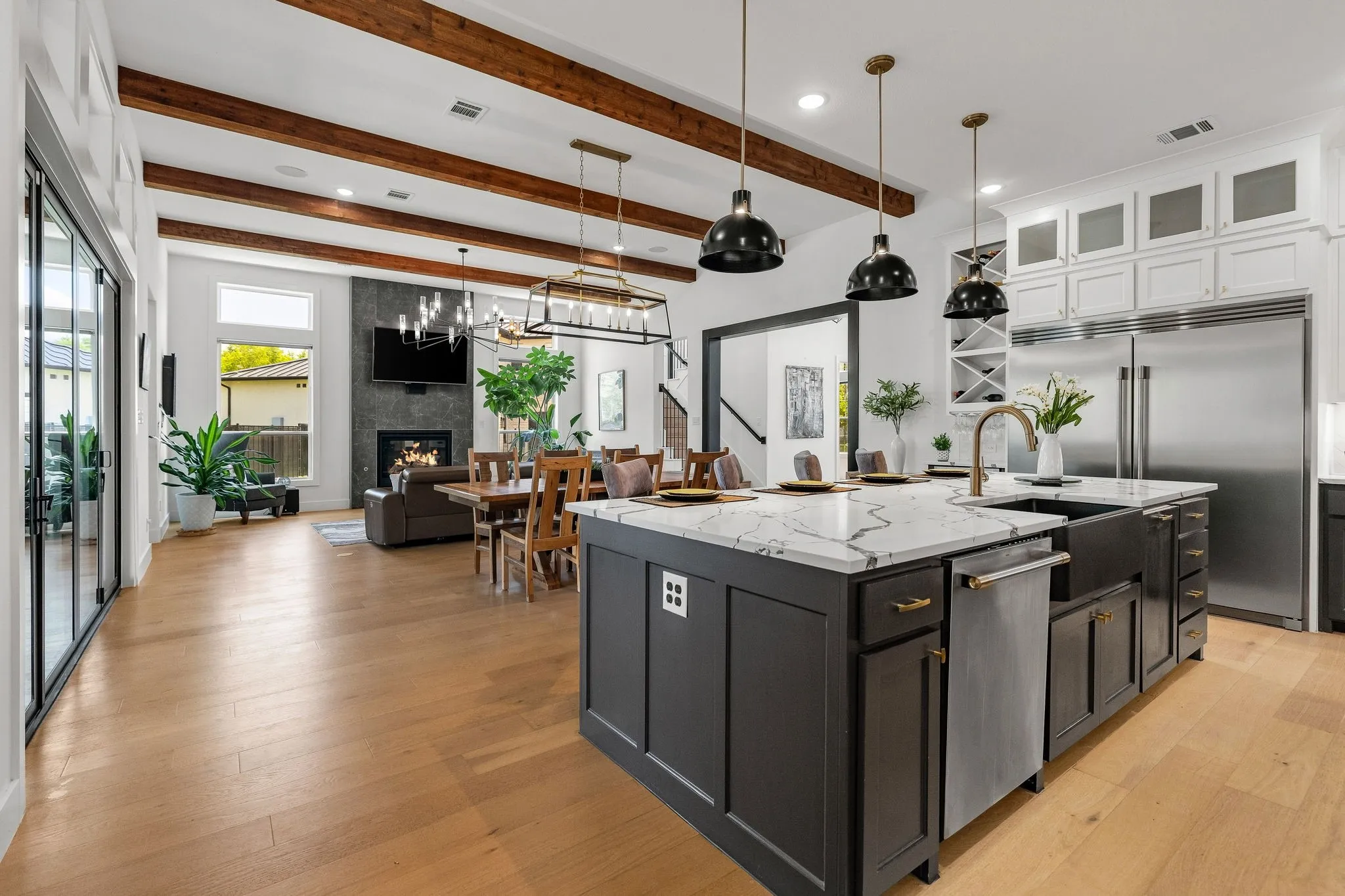 Open concept living space featuring wood-finish flooring, exposed ceiling beams, and a modern kitchen island with a farmhouse sink