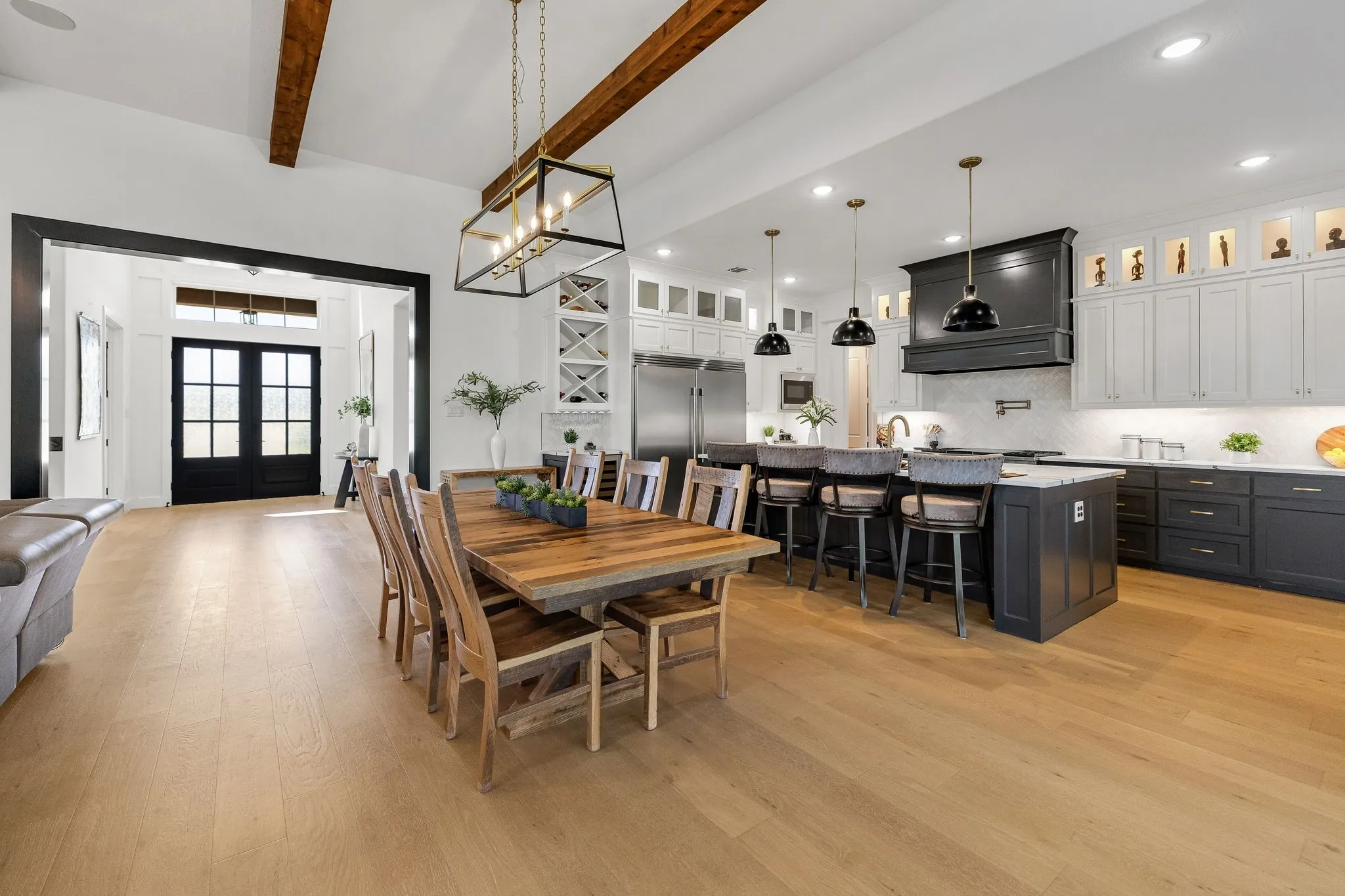 Vaulted ceilings with exposed wood beams, light wood-finish flooring, two-tone cabinetry, kitchen island with seating, and a decorative ceiling light fixture
