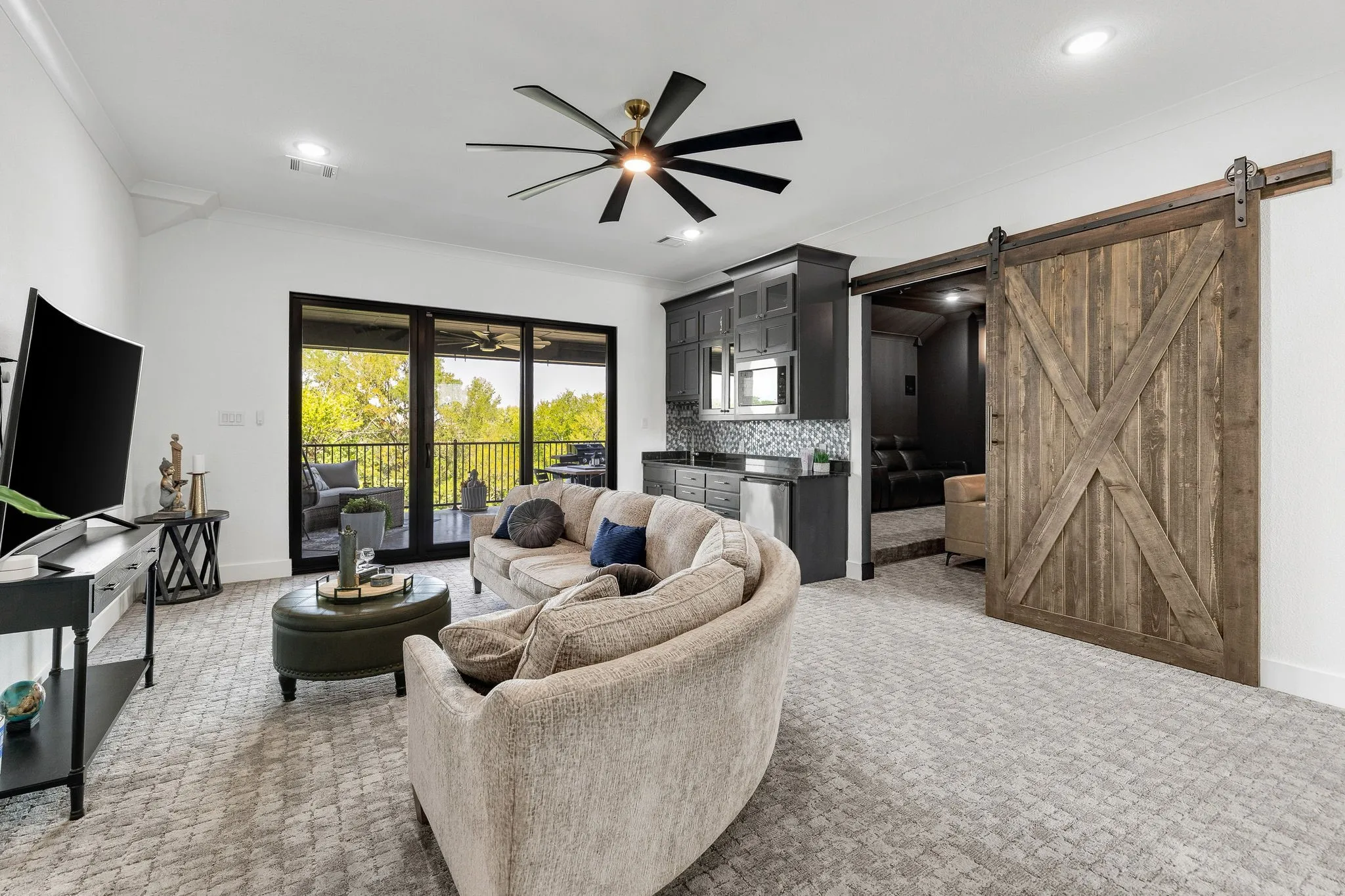 Recessed lighting, ceiling fan, built-in wet bar with mosaic tile backsplash, wood barn door, and glass sliding doors to an outdoor area