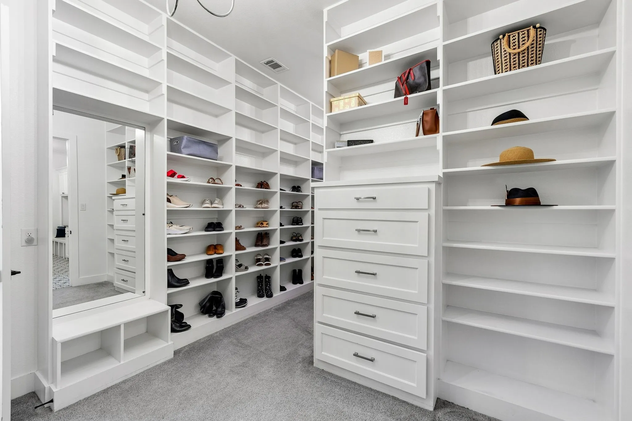 Luxurious walk-in closet featuring extensive white cabinetry with multiple shelving units, integrated drawers, and a mirrored accent wall