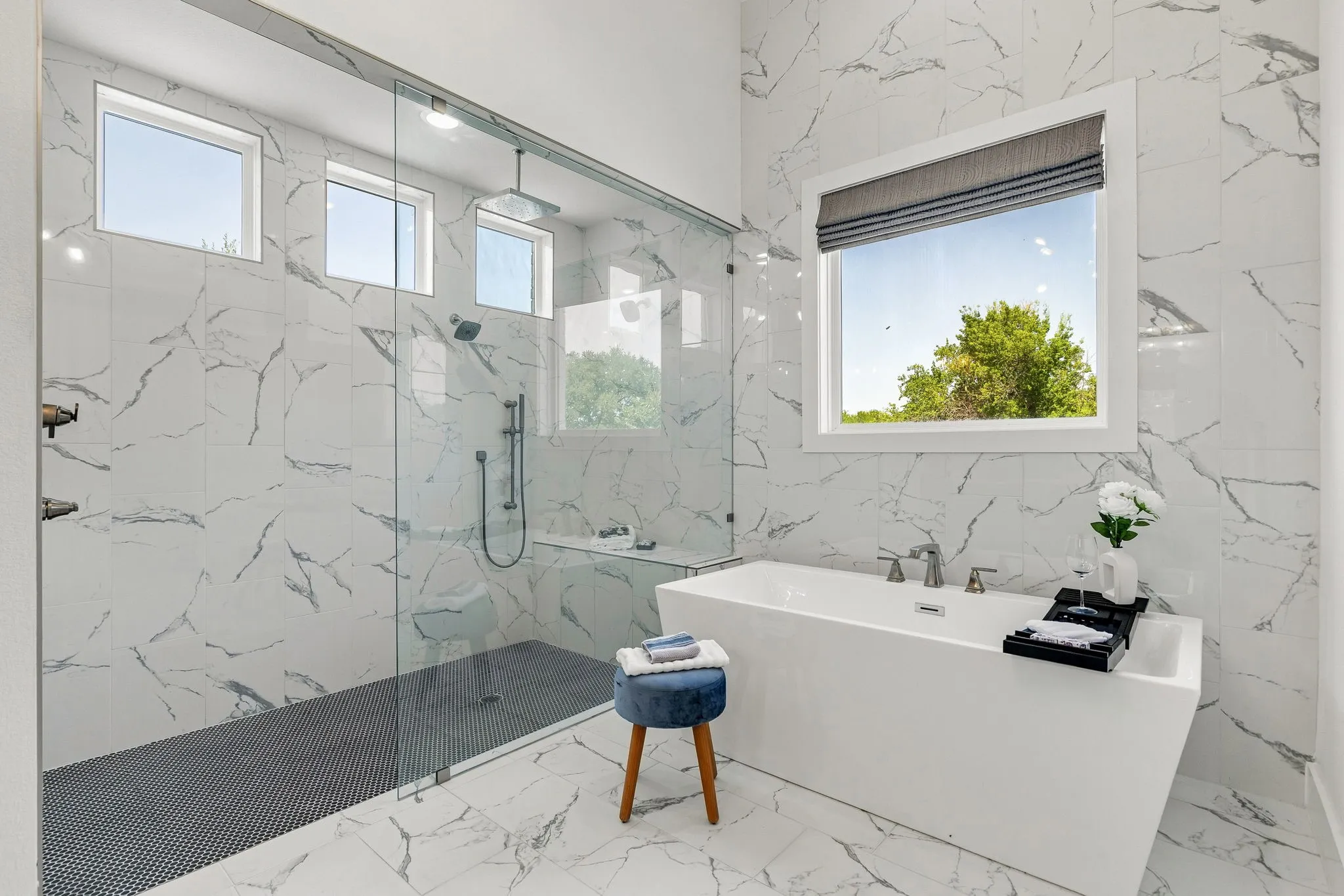 Freestanding soaking tub with polished chrome fixtures, walk-in shower with glass enclosure, rain shower head, and bench seating