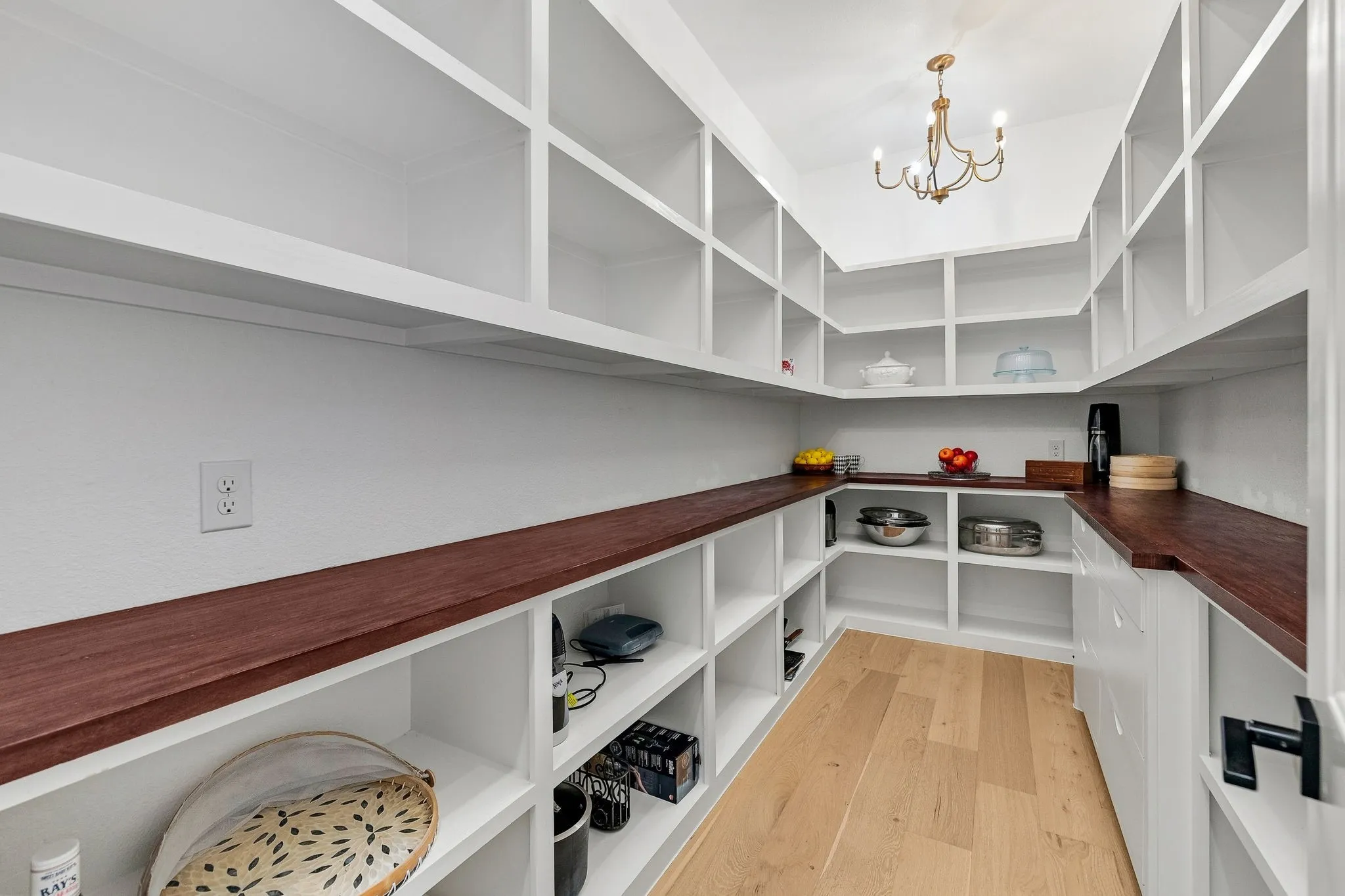 Expansive pantry featuring extensive built-in shelving, dark wood-finish countertops, light wood-finish flooring, and an overhead chandelier