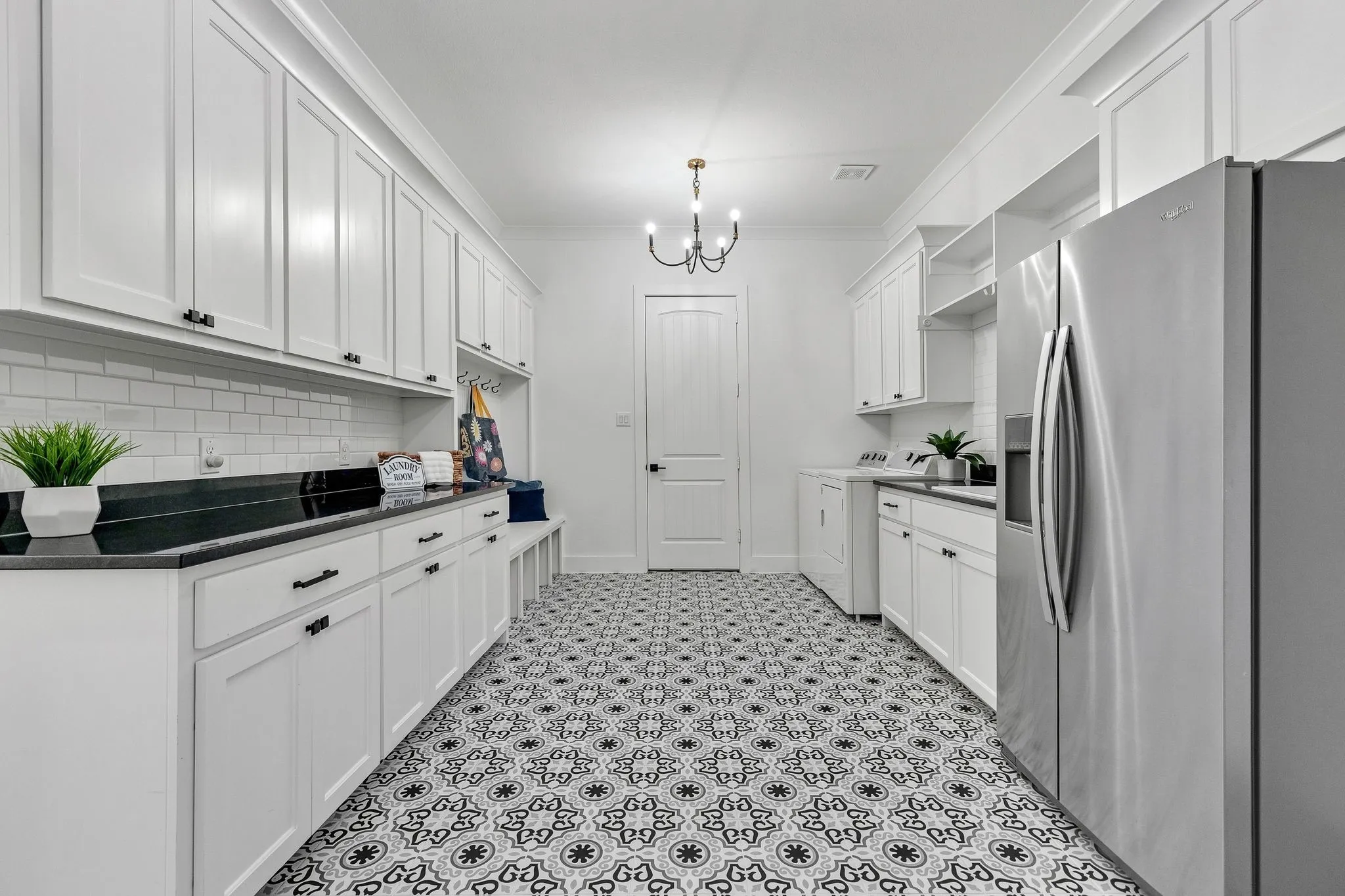White cabinetry, black countertops, patterned floor tiling, subway tile backsplash, and a black chandelier