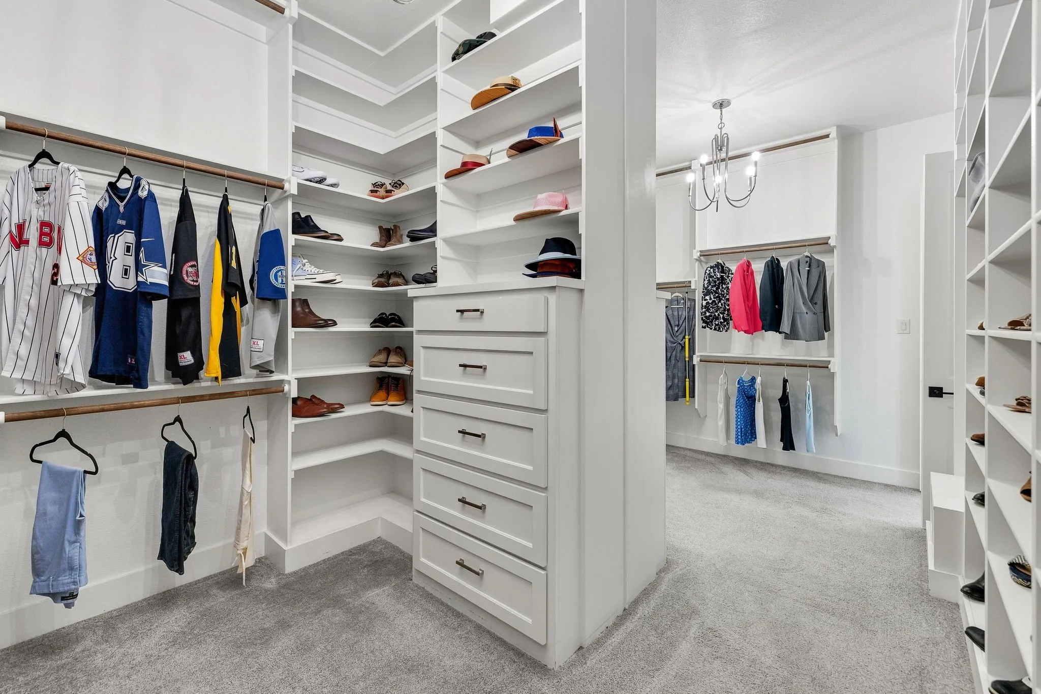 Custom built-in white shelving, integrated drawers with dark hardware, multiple hanging rods, corner shelving units, and a central chandelier