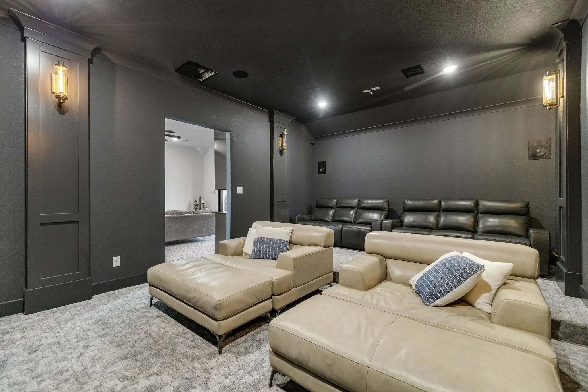 Recessed lighting illuminating the dark ceiling, wall sconces with gold-toned accents, and paneled walls in a deep gray finish