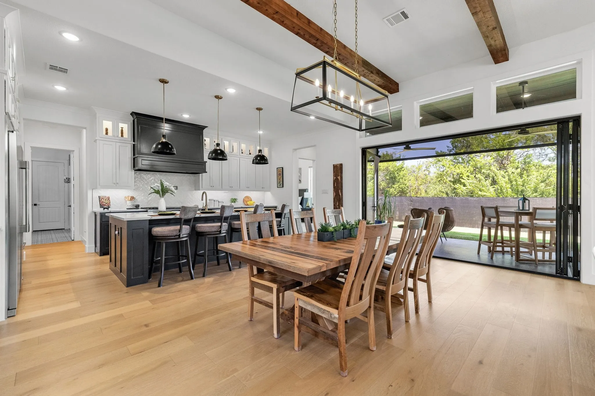 Hardwood flooring throughout, kitchen with large island, exposed ceiling beams, folding glass doors, and transom windows