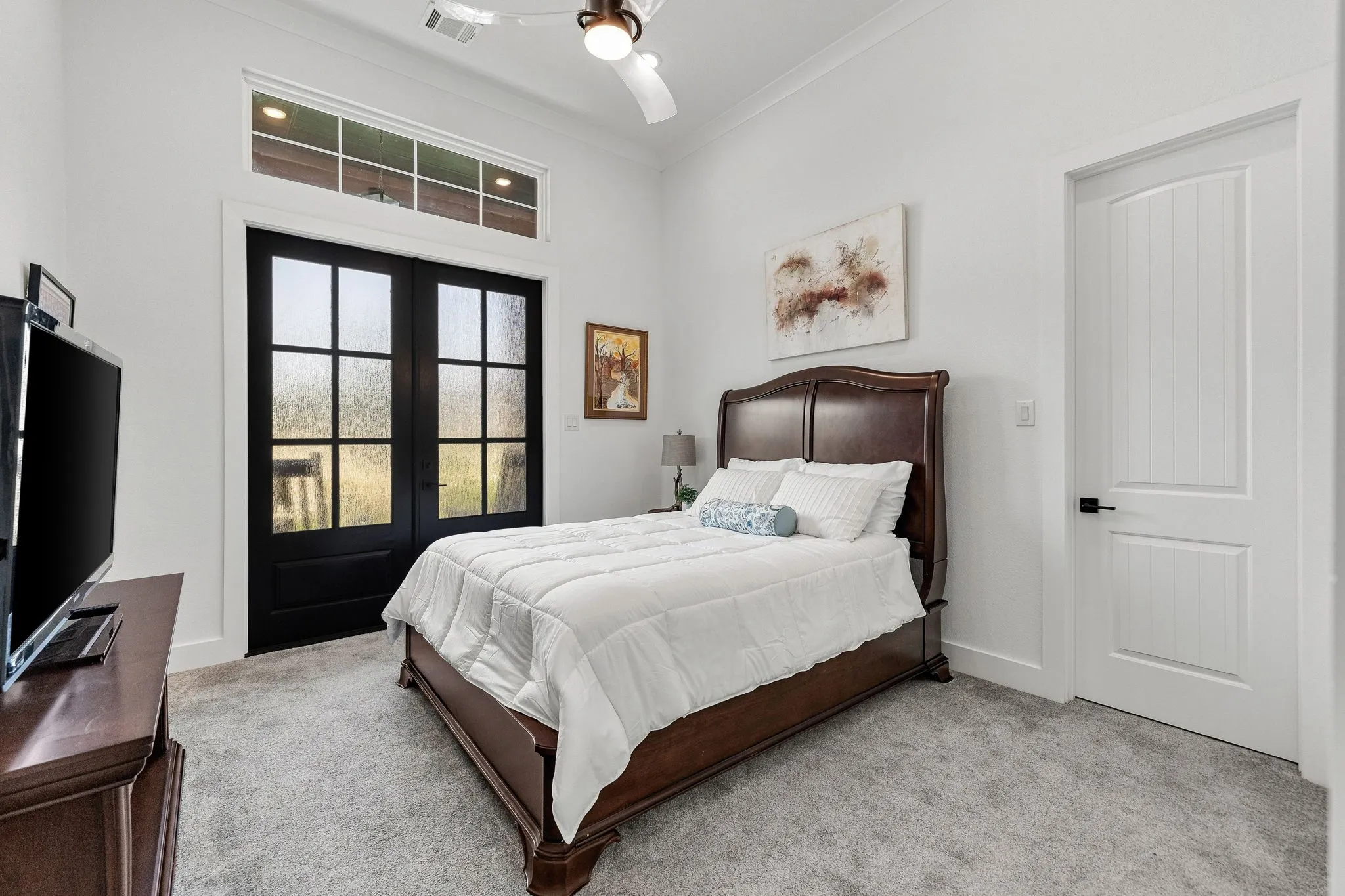 Spacious secondary bedroom featuring a wood-finish bed frame, soft-gray carpeting, and abundant natural light from French doors