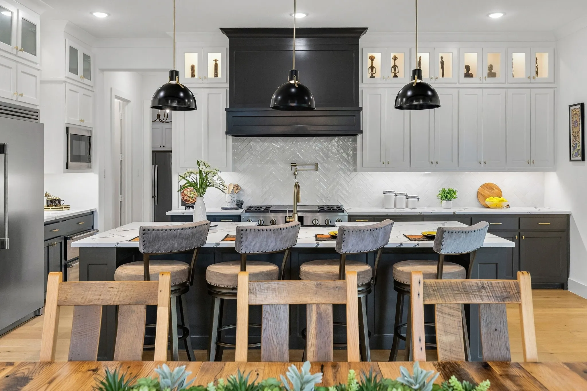 Gourmet kitchen featuring a large central island, a custom range hood, stainless steel appliances, and abundant cabinetry with glass-front accents