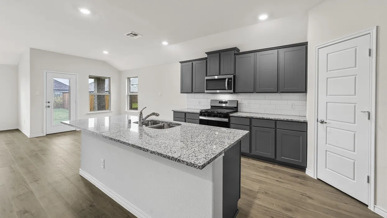 Kitchen island with integrated sink, wood-finish flooring, dark cabinetry, stainless steel appliances, and white subway tile backsplash