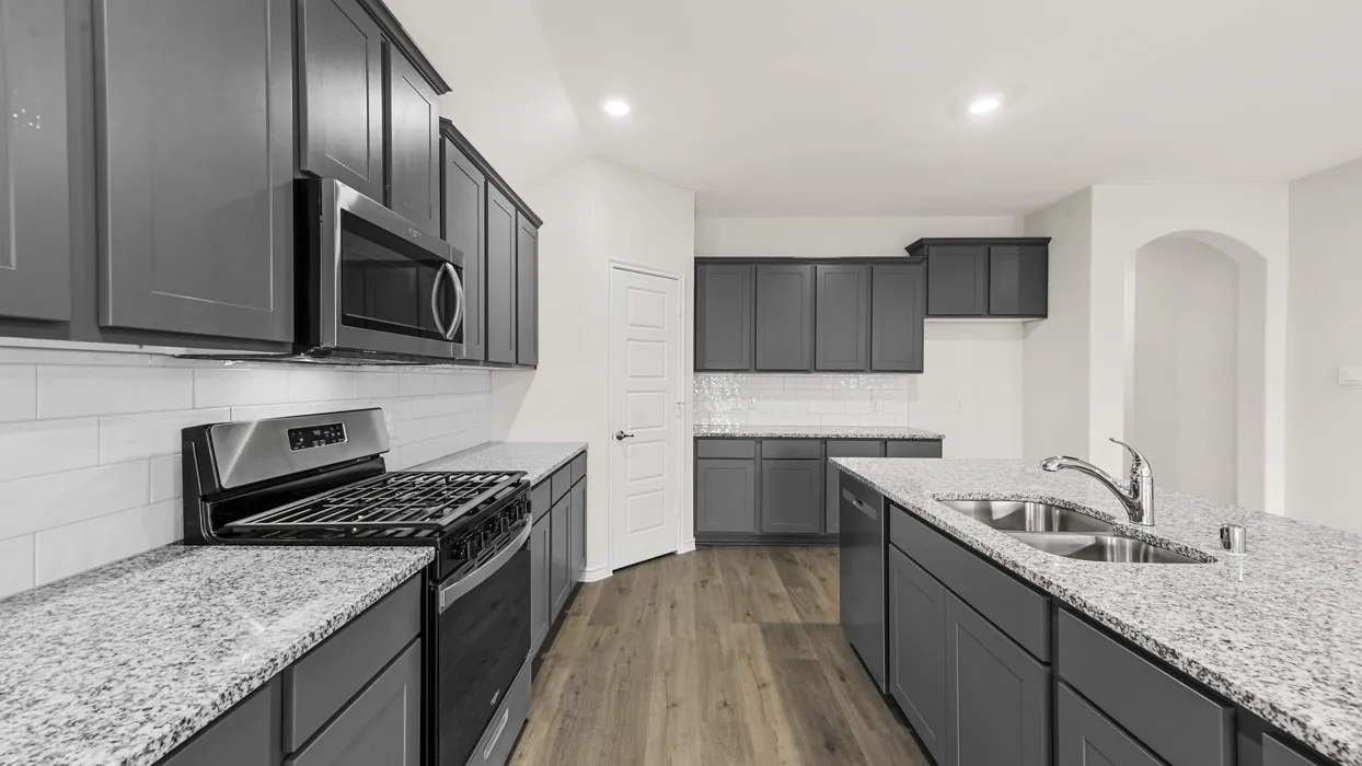 Modern kitchen featuring dark cabinetry with shaker-style doors, quartz countertops, stainless steel appliances including a gas range and built-in microwave, white subway tile backsplash, and wood-finish flooring throughout the open layout