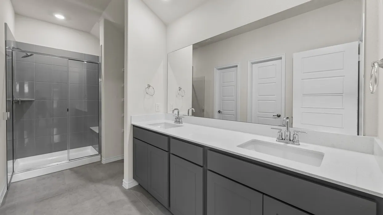 Dual vanity with undermount sinks, expansive wall-mounted mirror, gray cabinetry, and a walk-in shower with a built-in bench