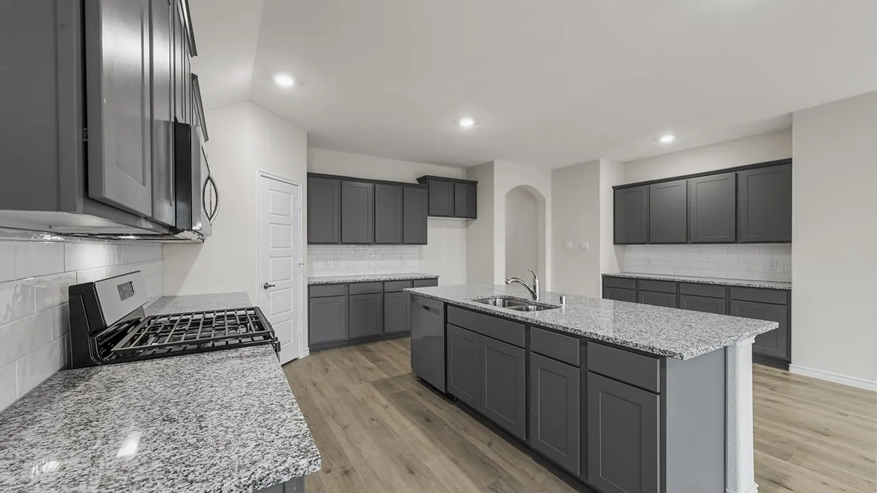 Kitchen featuring an island with an integrated sink, gray cabinetry, speckled countertops, a subway tile backsplash, and wood-finish flooring