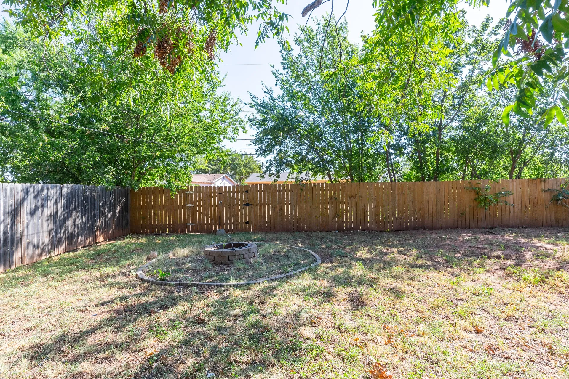 Expansive backyard featuring a wood privacy fence and a built-in fire pit with stone surround