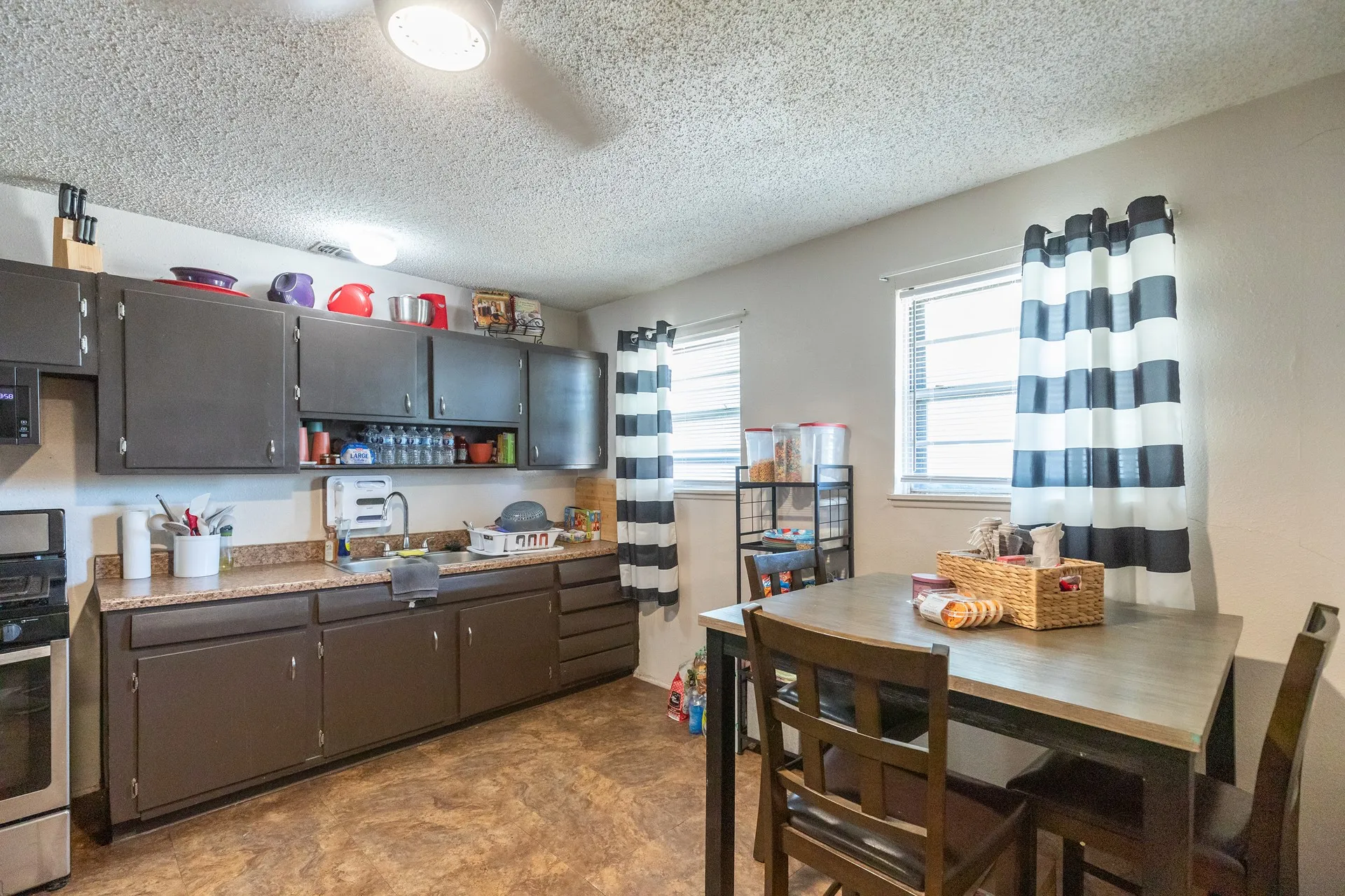 Kitchen featuring dark wood-finish cabinetry, light-toned countertops, a stainless steel range, and two windows providing natural light