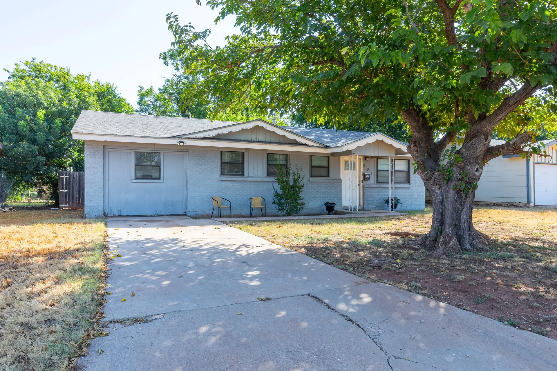 Single-story residence with a paved driveway, front porch with decorative columns, and mature tree
