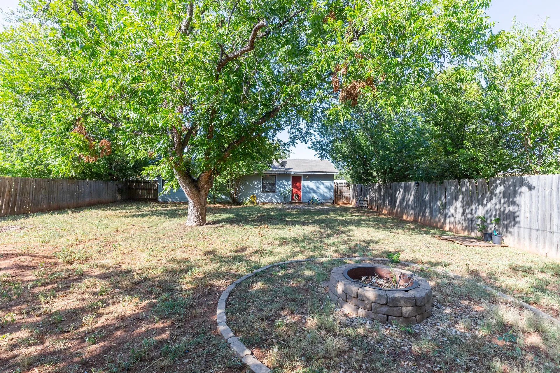 Expansive backyard featuring mature trees, a wood privacy fence, and a stone-lined fire pit