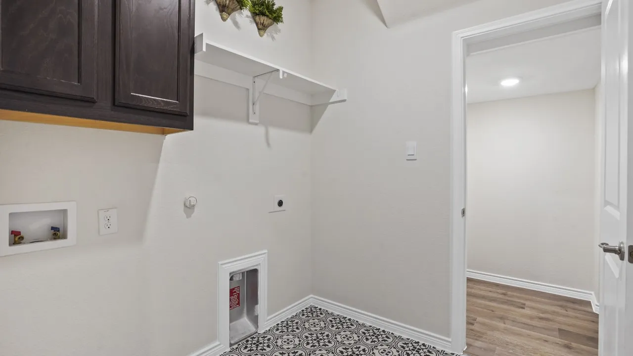 Dedicated laundry room featuring dark cabinetry with upper storage, white subway tile backsplash, patterned tile flooring, wall-mounted utility sink, and direct access to adjacent spaces
