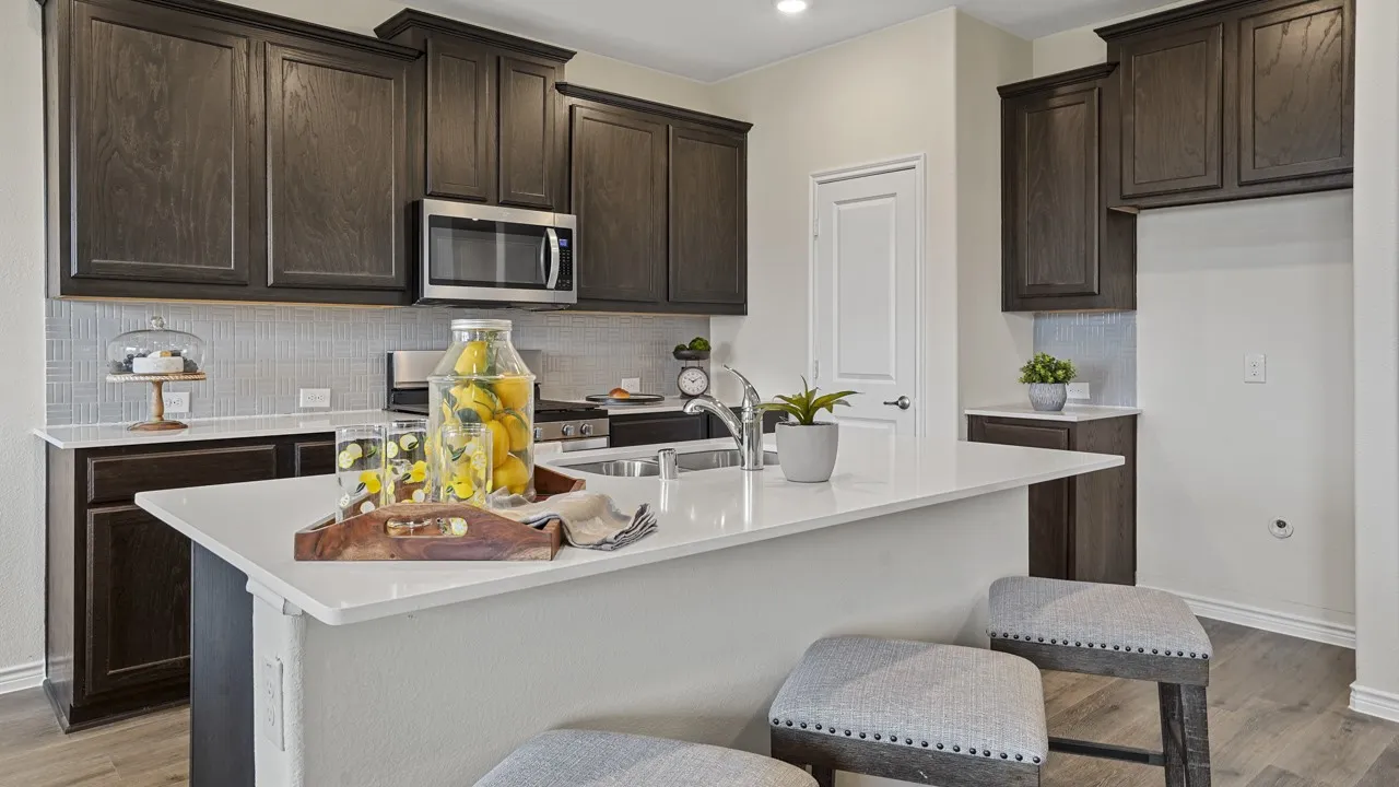 Kitchen featuring dark wood-finish cabinetry, stainless steel microwave, light-toned countertop island, and light tile backsplash
