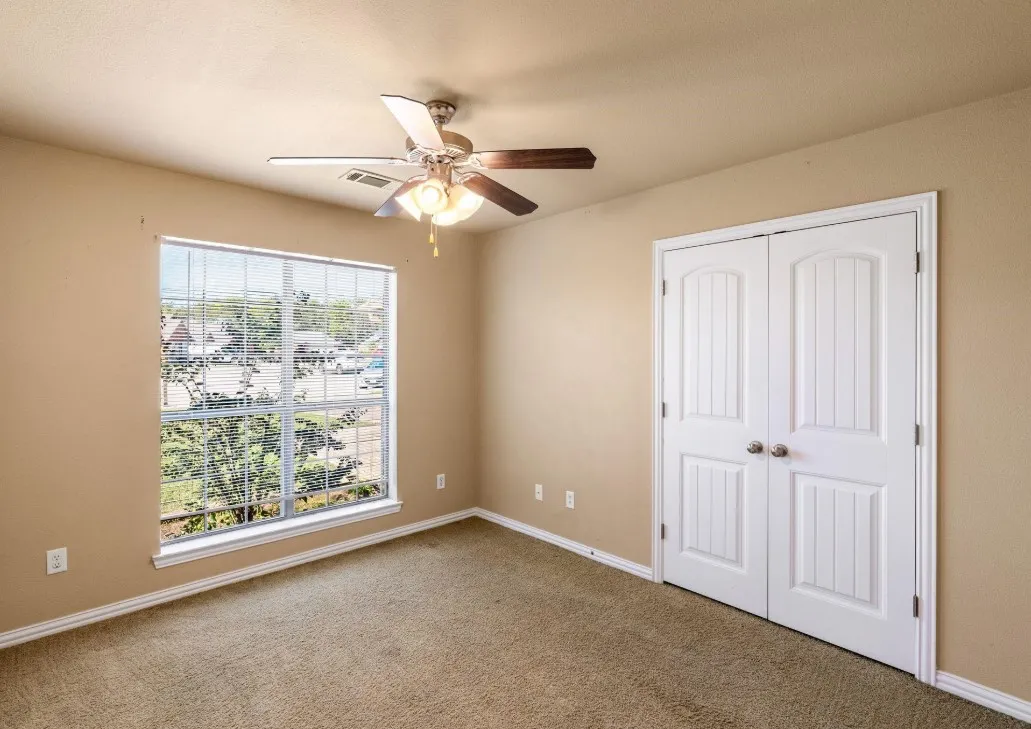 Textured carpeting, neutral wall tones, white trim, recessed window, and a ceiling fan with integrated lighting