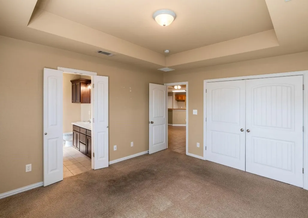Tray ceiling with flush mount lighting, white paneled bifold doors, and an additional room with a dark wood vanity and wall cabinet