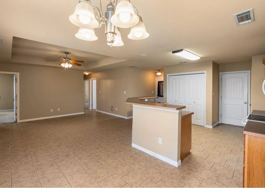 Tray ceiling with a ceiling fan, tiled flooring, built-in breakfast bar, and white bi-fold closet doors