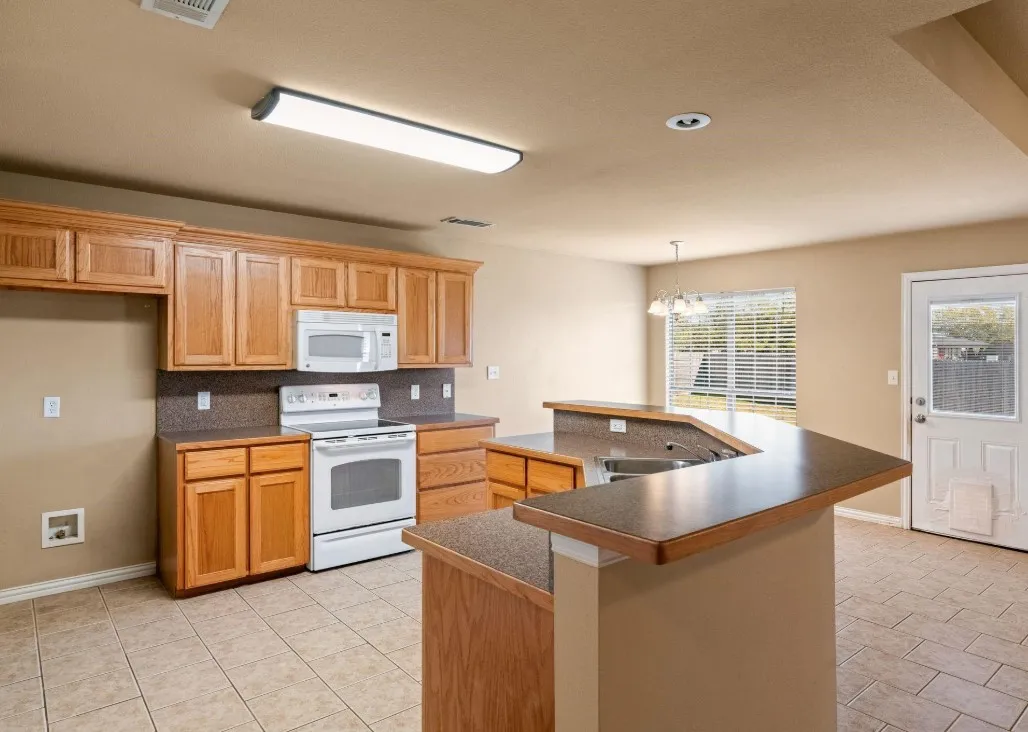 Kitchen featuring a breakfast bar, wood-finish cabinetry, tile flooring, and a white appliance package