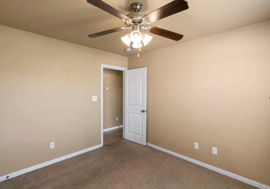 Ceiling fan with integrated lighting, neutral wall tones, carpeted flooring, white trim, and a paneled interior door