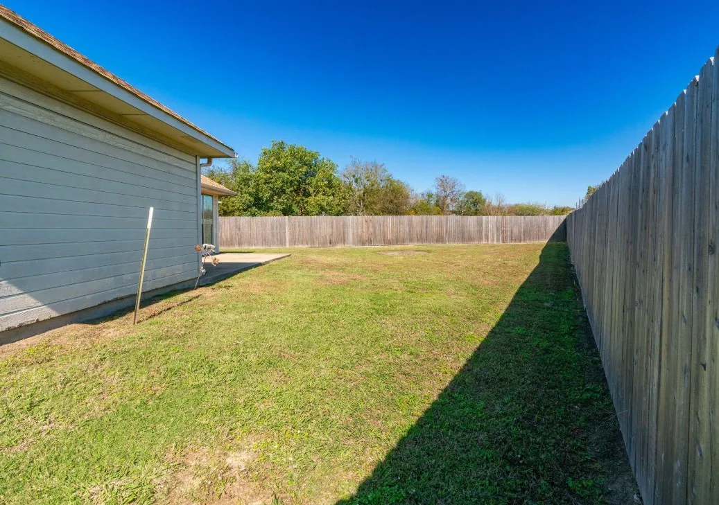 Expansive grass lawn with a full privacy fence and a concrete patio