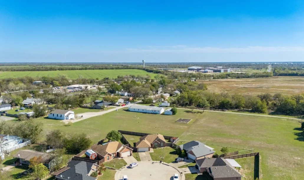 Residential cul-de-sac with various home styles, surrounded by expansive green spaces and distant agricultural fields