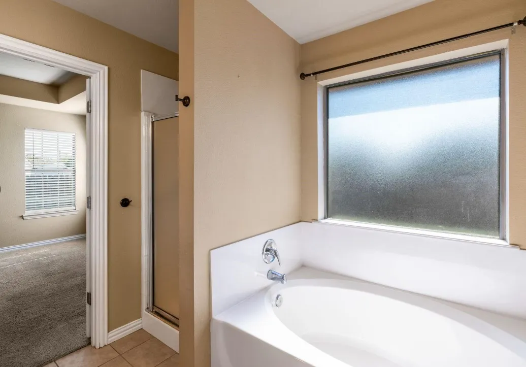 Soaking tub with a polished chrome faucet, tiled flooring, and a glass-enclosed shower