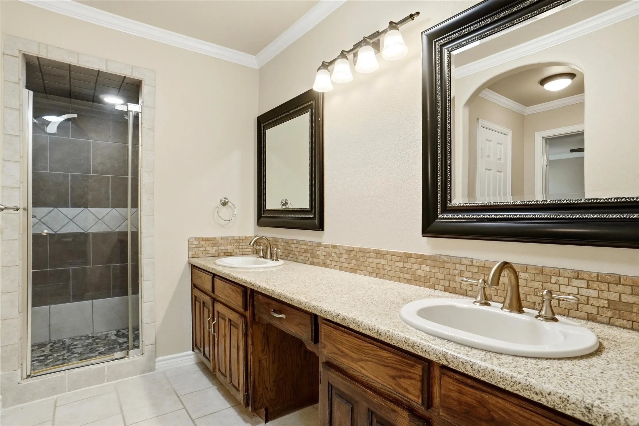 Dual vanity with wood cabinetry, speckled countertop, and subway tile backsplash
