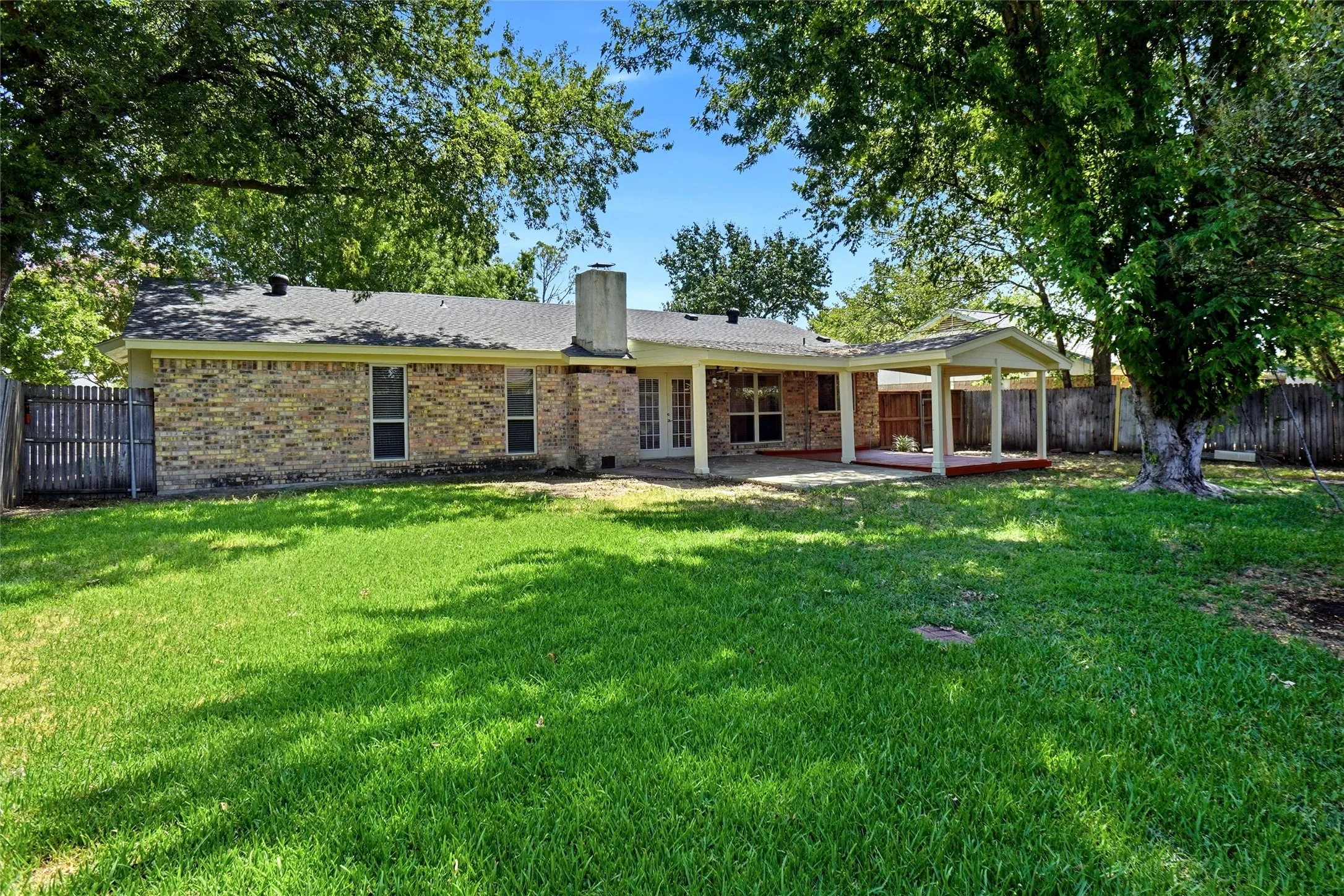 Expansive backyard featuring a manicured lawn, a covered patio, and mature trees