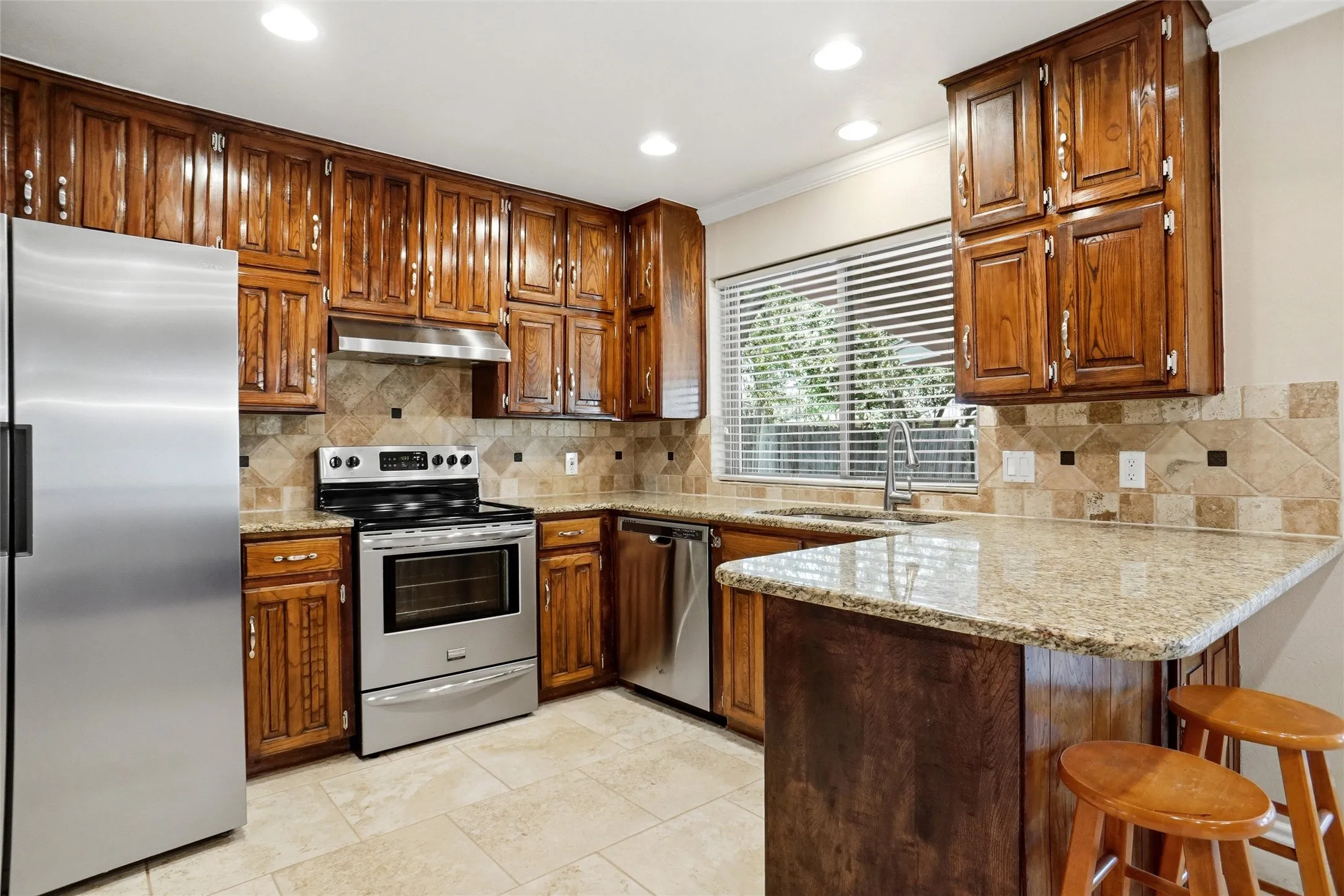 Kitchen featuring wood cabinetry, stainless steel appliances, tile flooring, and a stone countertop with breakfast bar seating